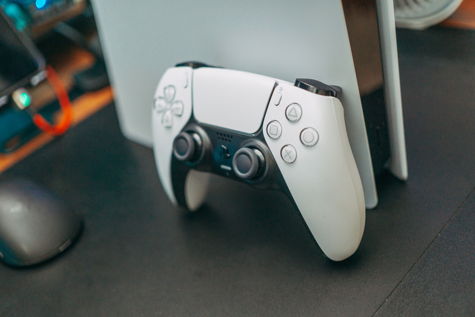 a gaming console and controller resting on a wooden desk next to a monitor showing a fictional sun-drenched coastal city environment