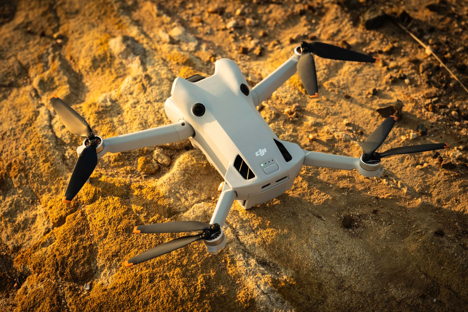 aerial view of an unmanned ground vehicle navigating a rocky outdoor testing track, with LiDAR sensor arrays visible mounted on its roof, dust rising in the background