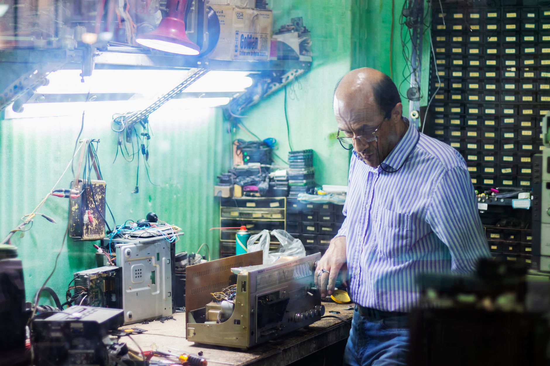rows of ruggedized electronic hardware modules on a workbench inside an engineering lab, with testing cables and diagnostic screens in the background