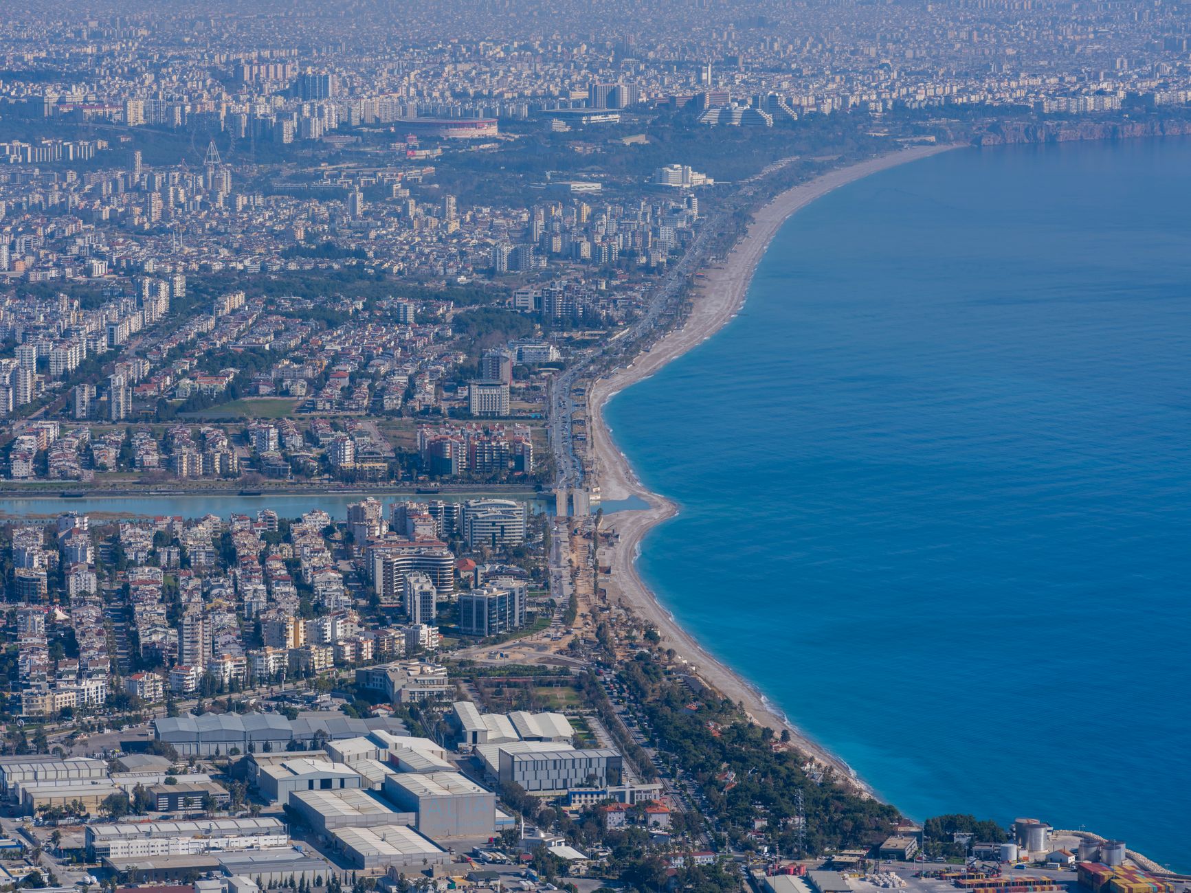 Wide aerial view of a Mediterranean naval base with concrete piers extending into blue water, no visible personnel