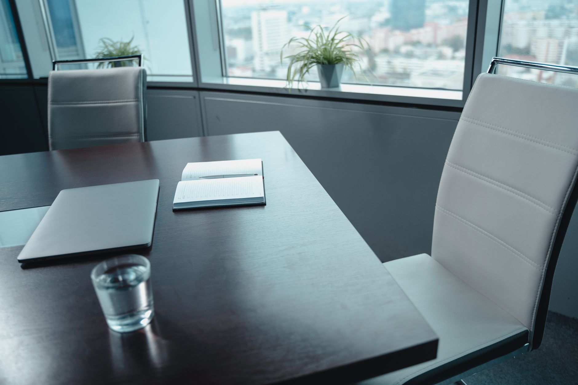 A sleek modern office conference room with glass walls overlooking a city skyline at dusk, a large monitor displaying a deal flow dashboard in the foreground