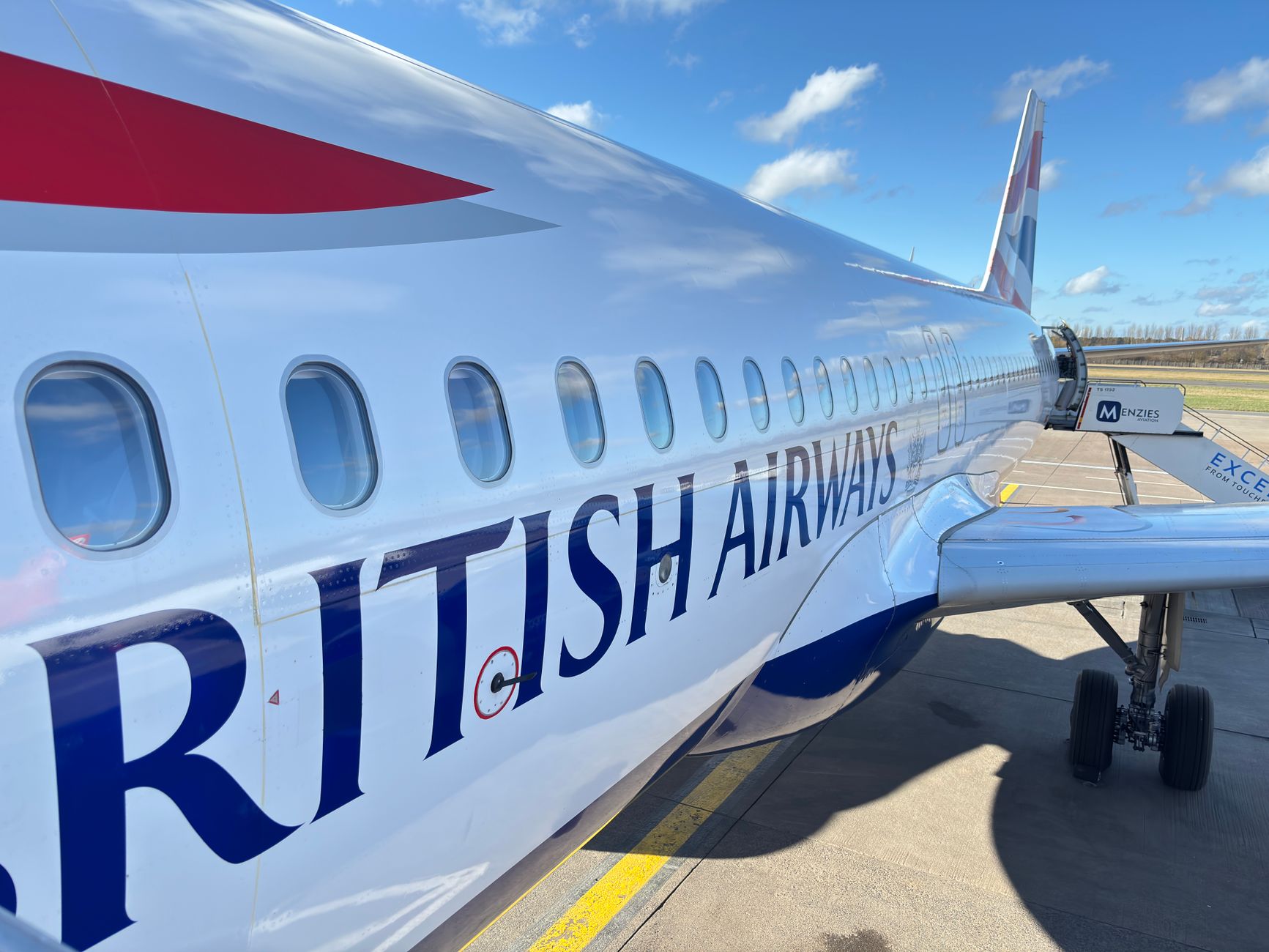 a modern commercial aircraft on a sunlit airport tarmac with a jet bridge extended and a clear blue sky overhead