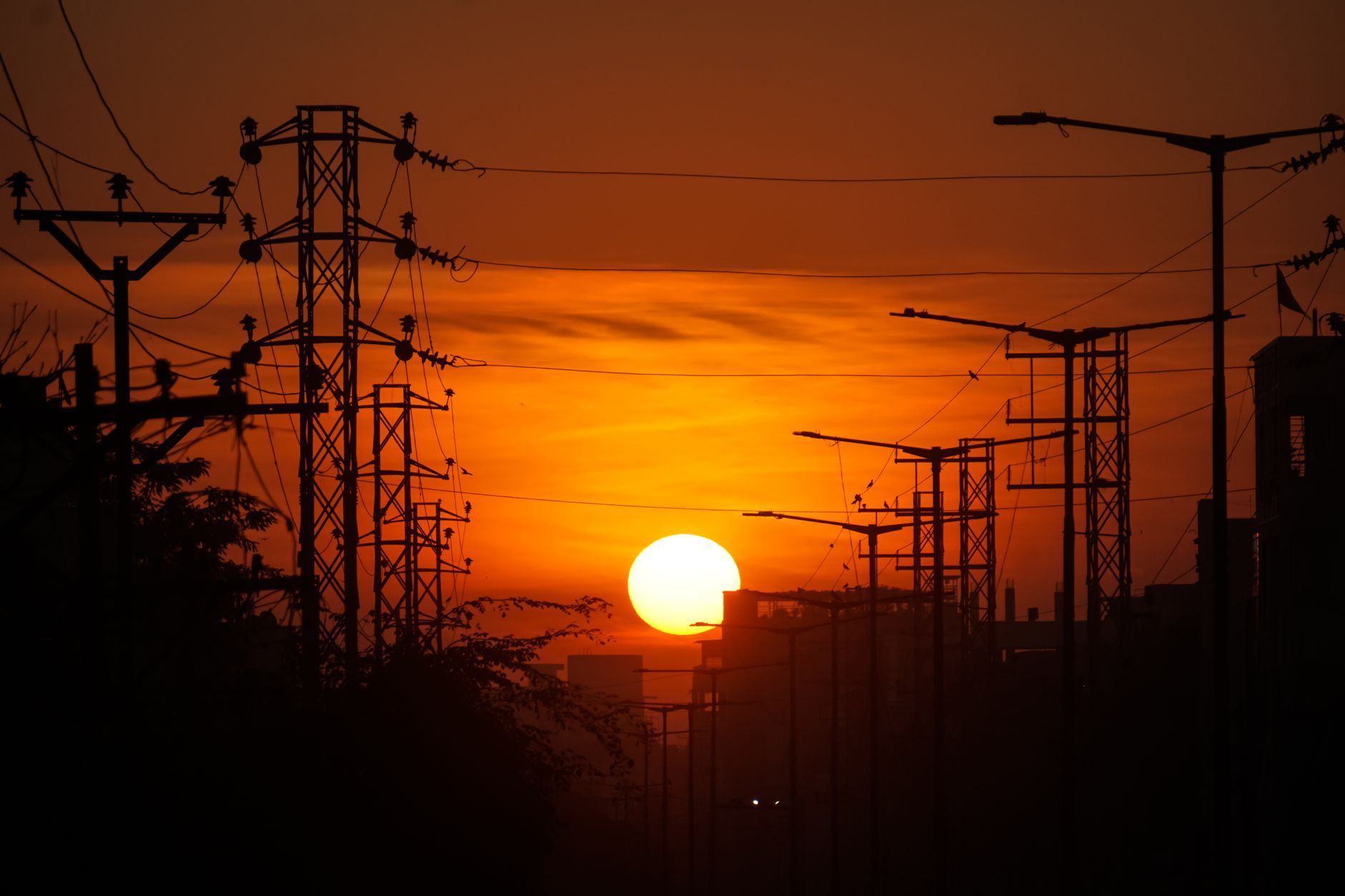 wide-angle view of a massive data center facility exterior at dusk, with cooling towers and power lines visible against an orange sky