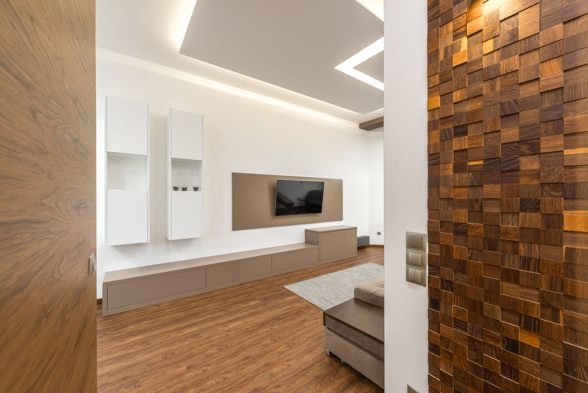 a sleek smart TV mounted on a living room wall displaying a streaming interface with rows of Indian film and series thumbnails, warm ambient lighting in the background