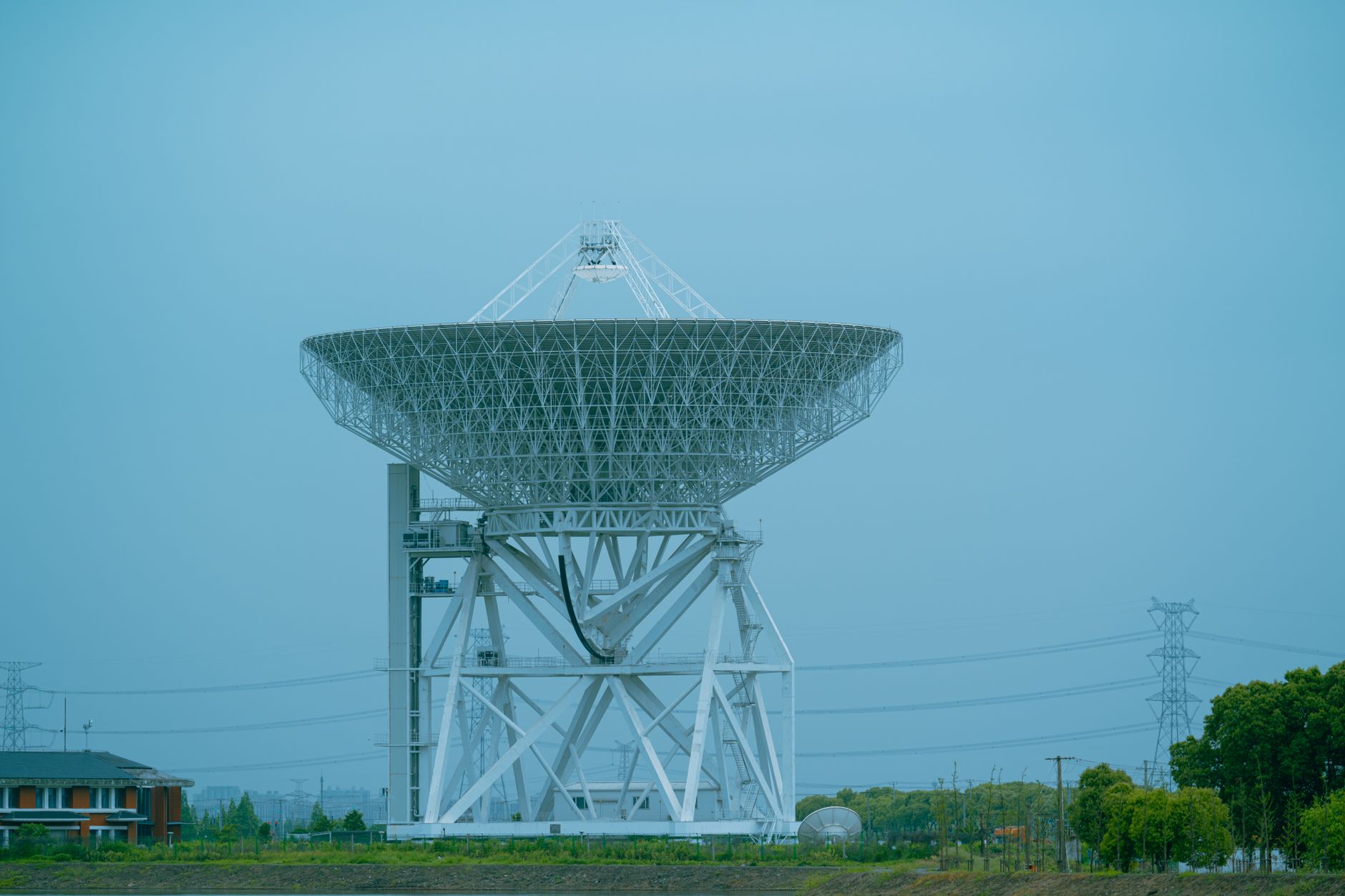 rows of satellite uplink dishes at a broadcast facility against a partly cloudy sky, with transmission equipment visible in the foreground