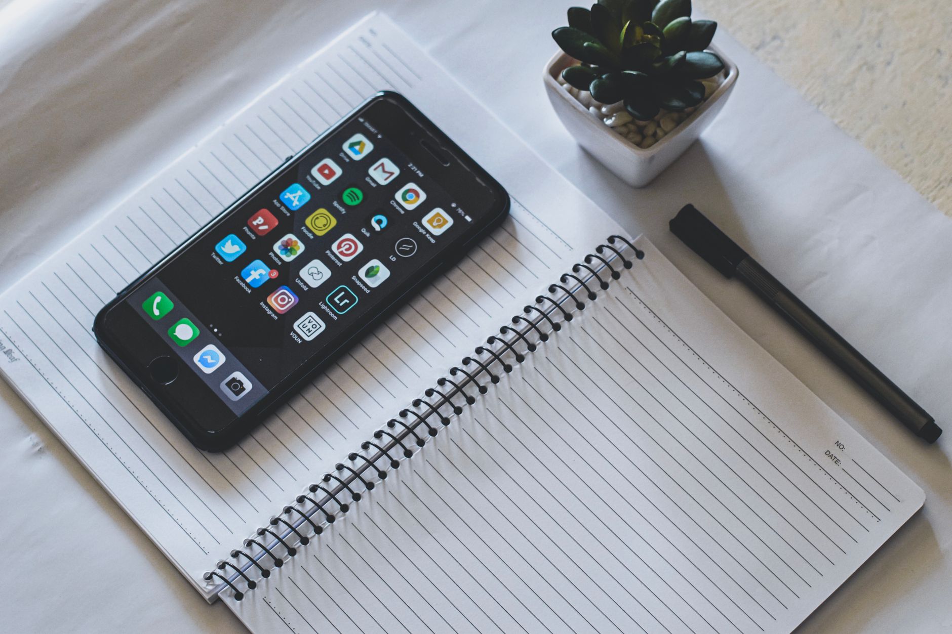 a smartphone screen displaying a social media feed with notification badges, resting on a wooden school desk beside a closed textbook