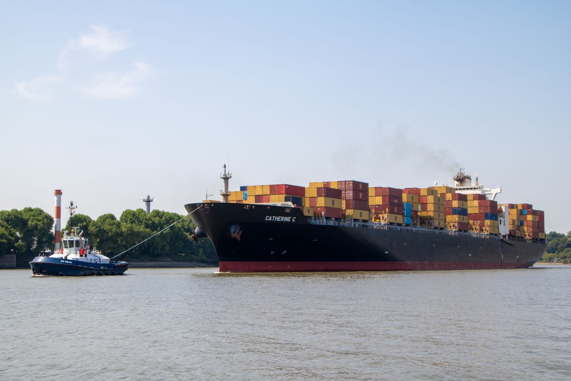 a large commercial container ship navigating through a busy shipping lane, viewed from an aerial perspective at dusk with port lights visible in the distance