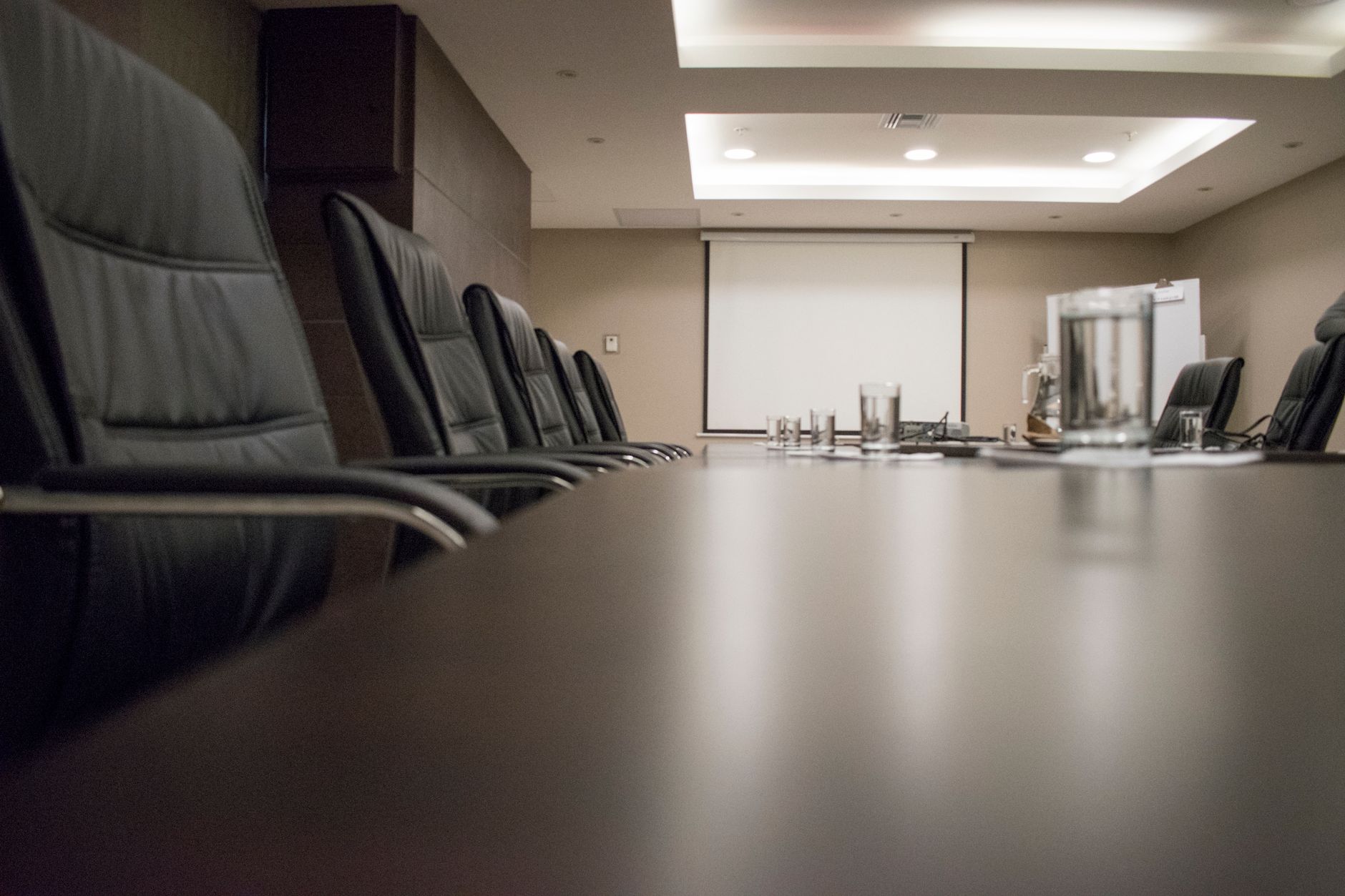 a modern glass-walled boardroom with a large monitor displaying financial graphs and business performance dashboards, empty chairs around a long conference table