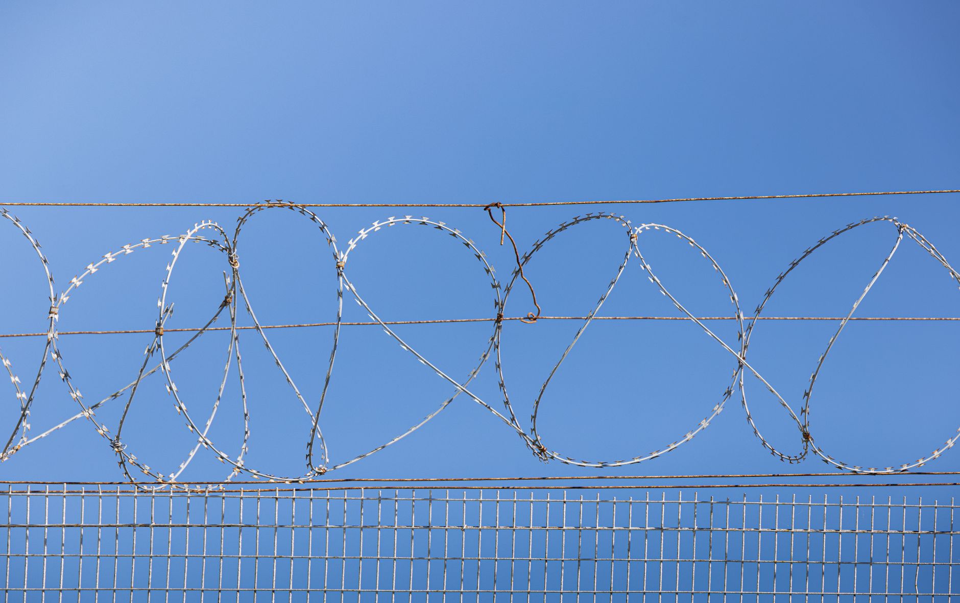 a secure government defense contractor facility exterior with reinforced fencing, satellite dishes, and surveillance equipment visible against a clear sky