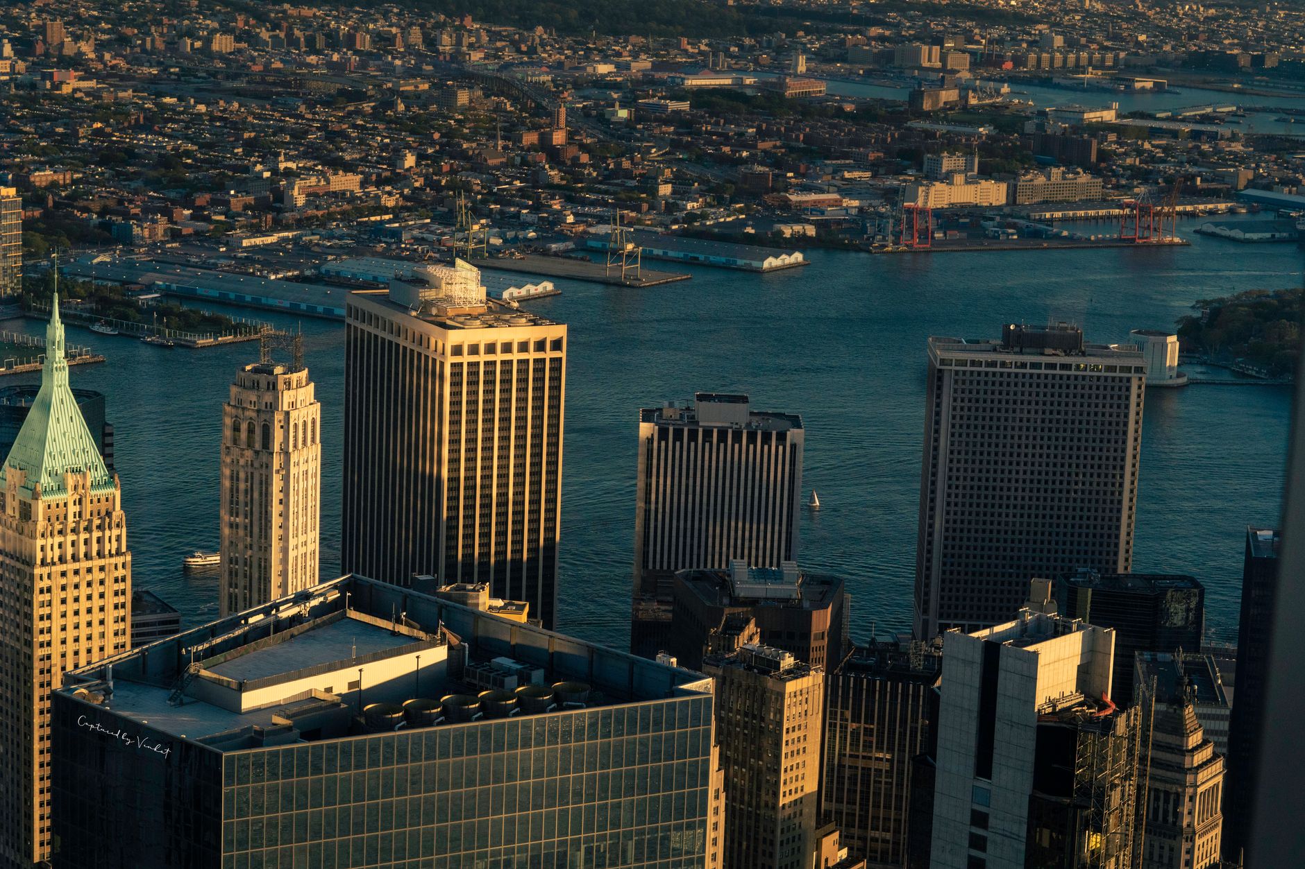aerial view of Lower Manhattan financial district skyline at dusk, glass towers reflecting orange light over the East River