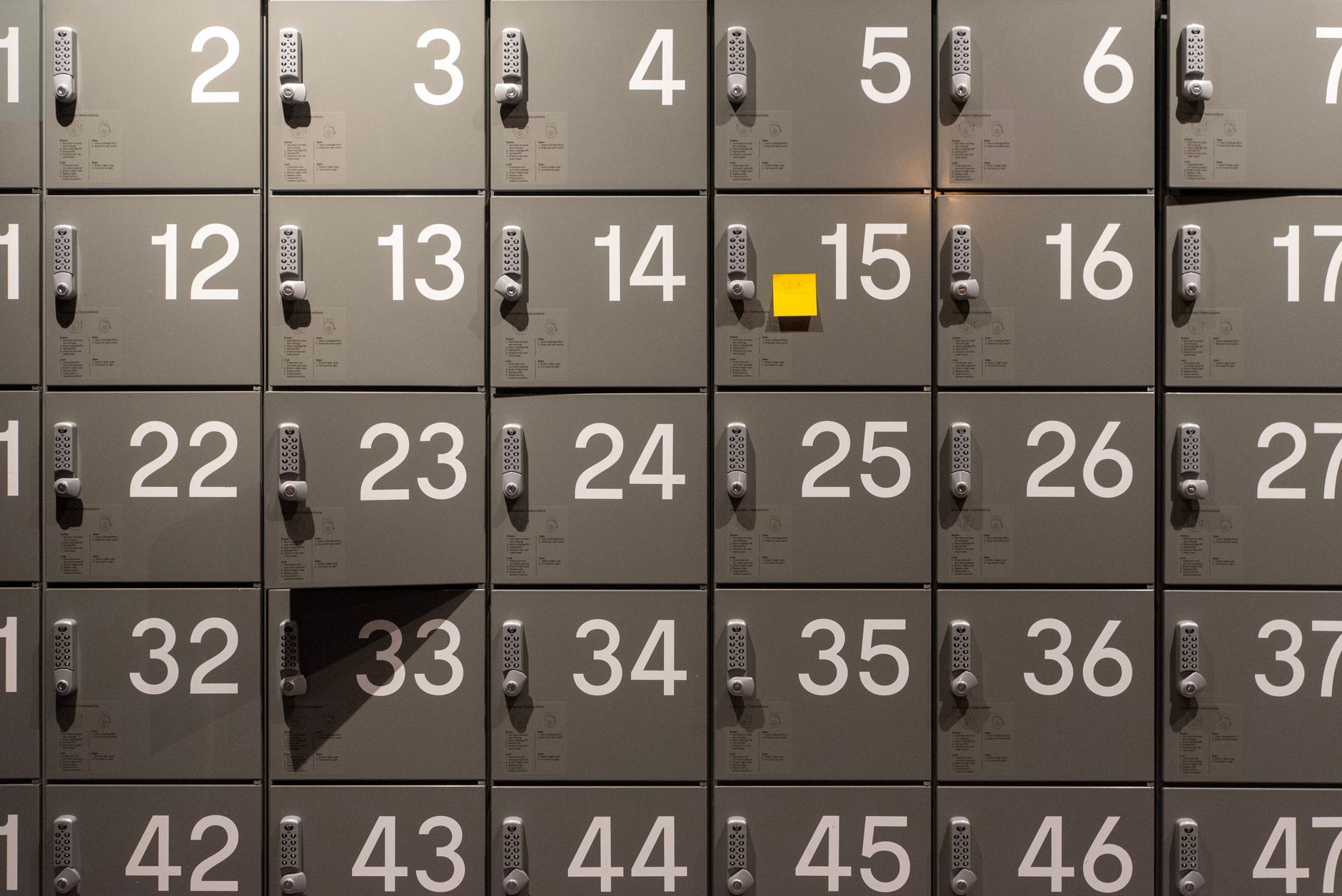 an empty school hallway with lockers lining the walls, yellow police tape stretched across a set of double doors at the far end, fluorescent lights flickering overhead