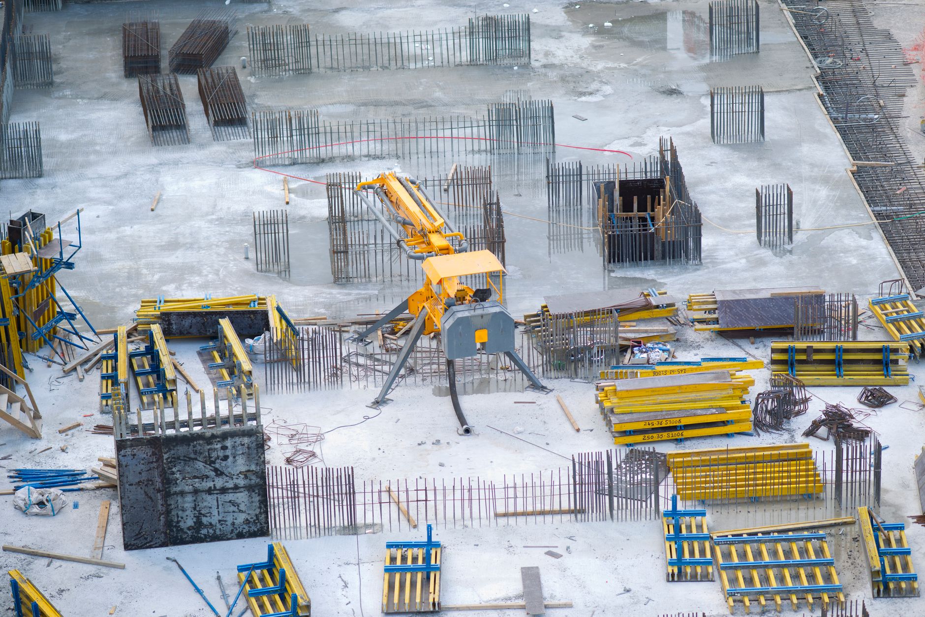 a wide-angle shot of a suburban school construction site with steel framework rising from a concrete foundation, surrounded by chain-link fencing and construction equipment
