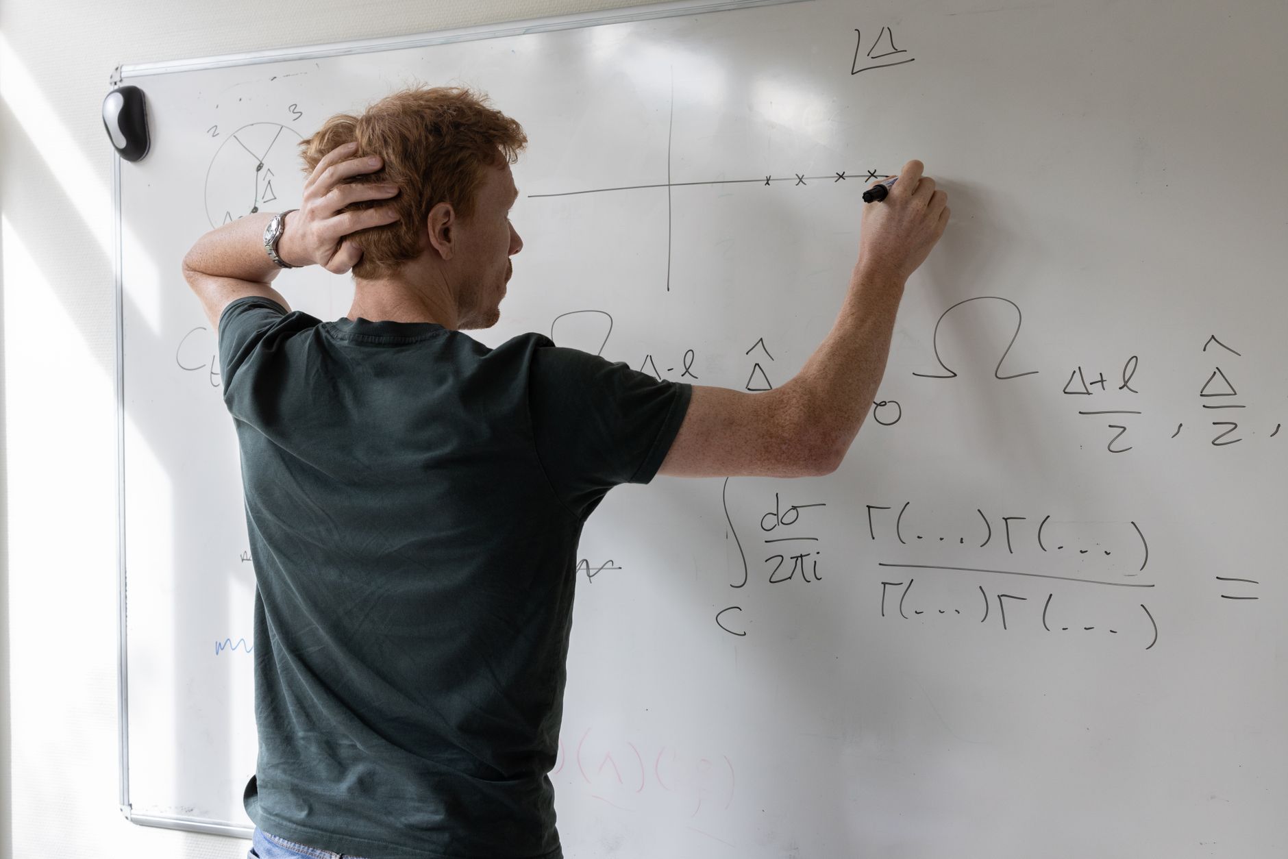 a whiteboard covered in dense mathematical equations and proofs inside a university research office, chalk dust visible on the tray below
