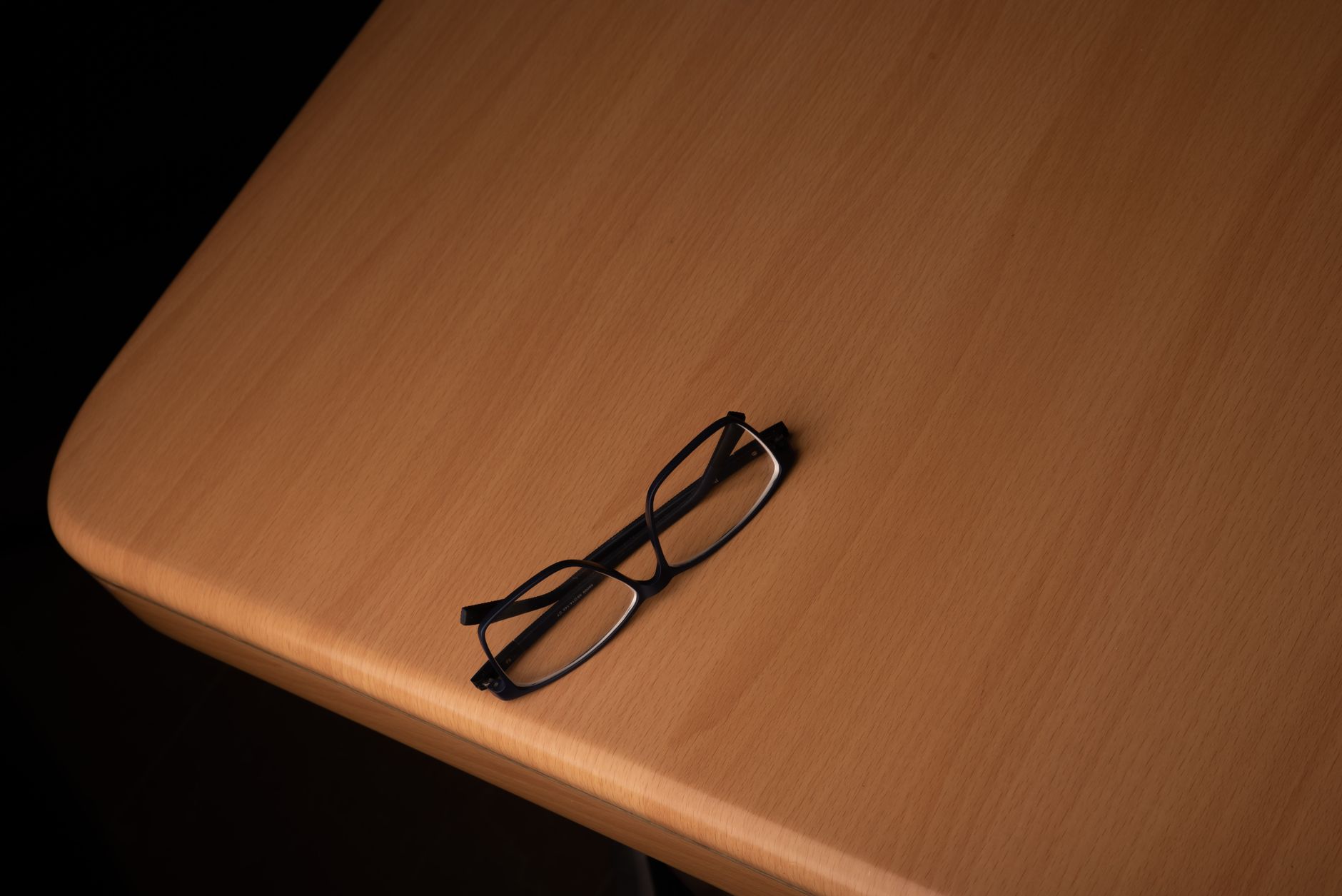 a pair of slim consumer smart glasses resting on a wooden surface next to a Qualcomm development board, shot in soft studio lighting