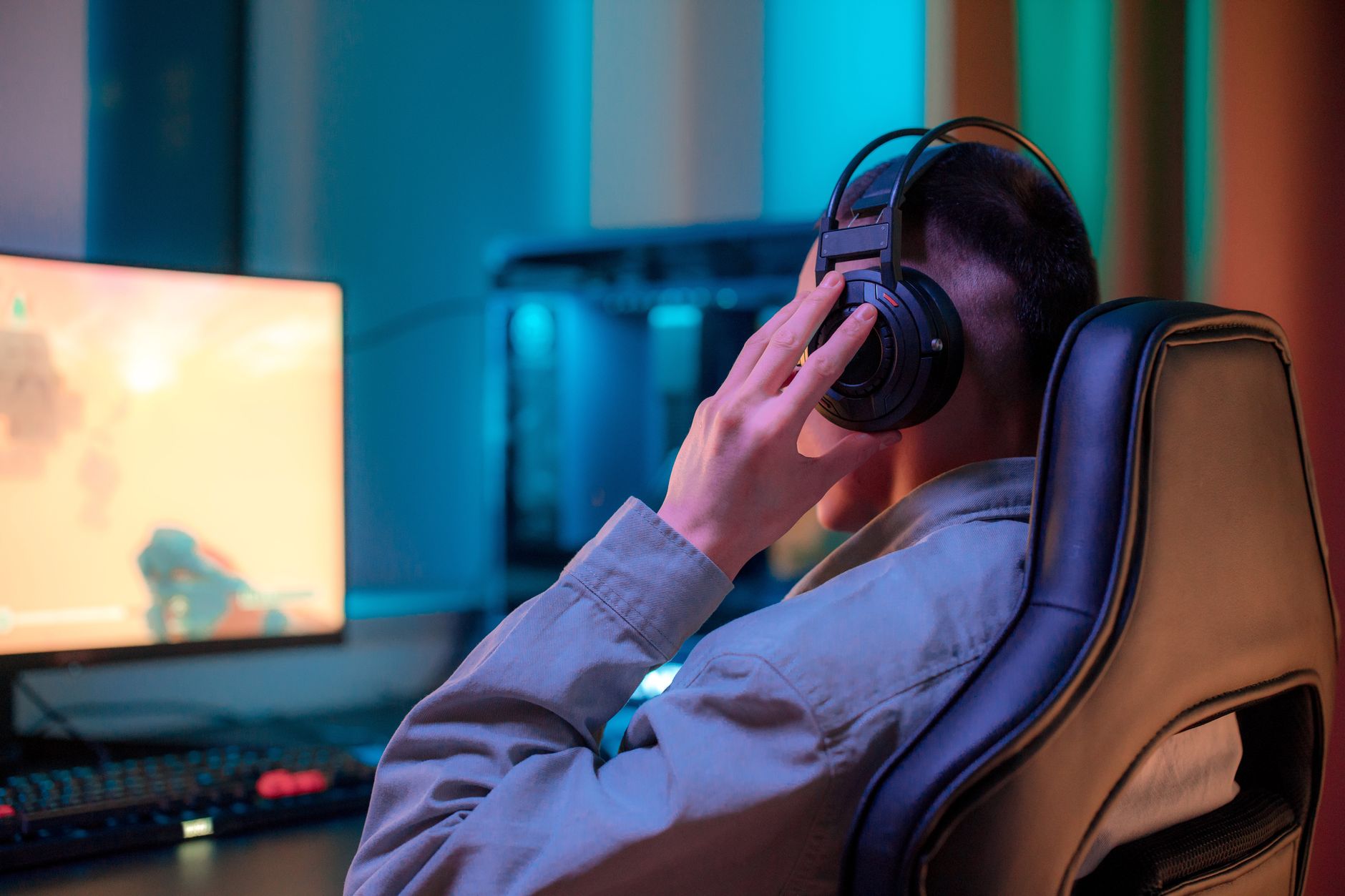 A gaming setup featuring a wireless headset placed on a headset stand beside a gaming console and monitor displaying a paused game interface, captured from a wide desk-level angle