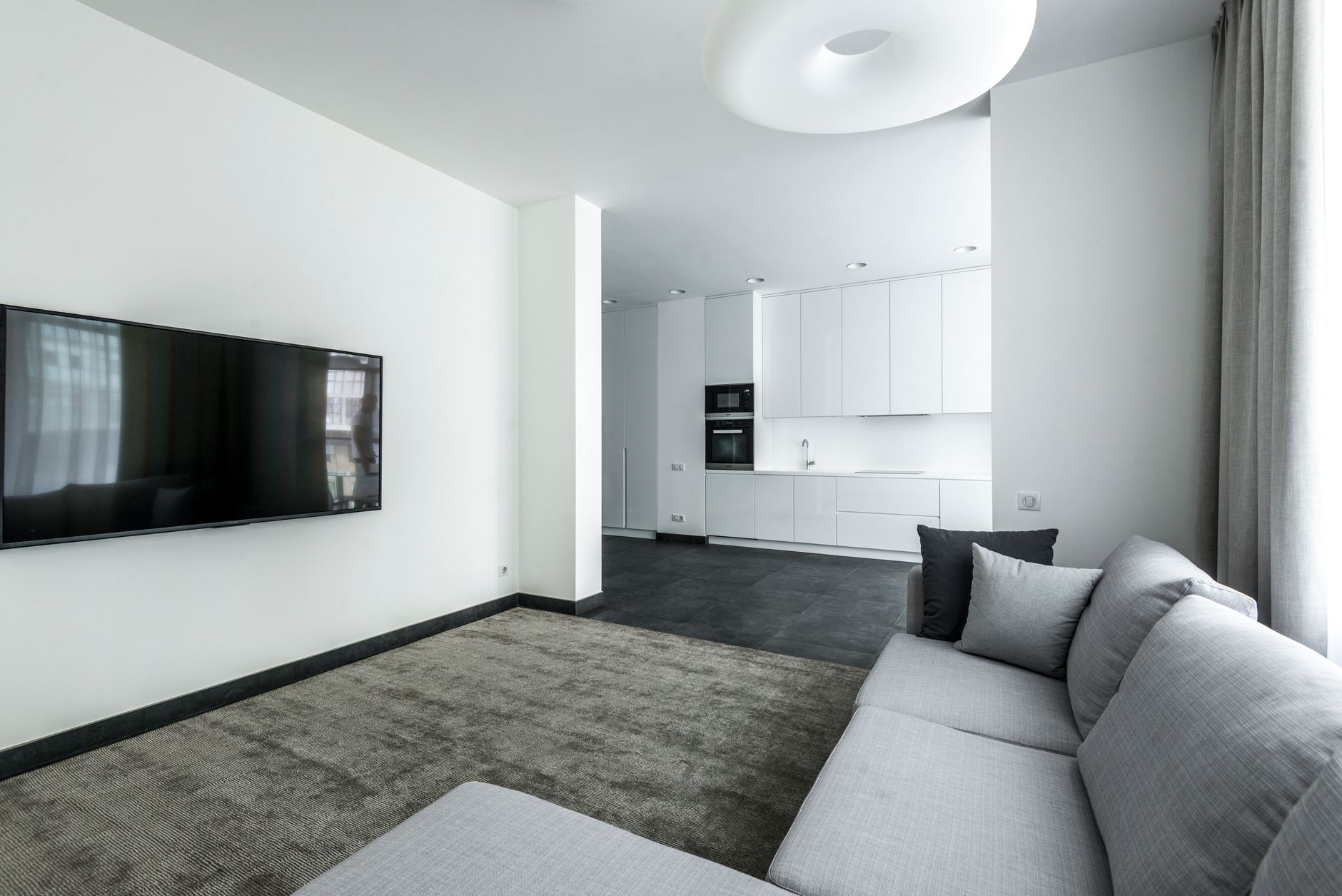 a large flat-panel OLED television mounted on a living room media console displaying a dark cinematic scene, with deep blacks visible across the screen