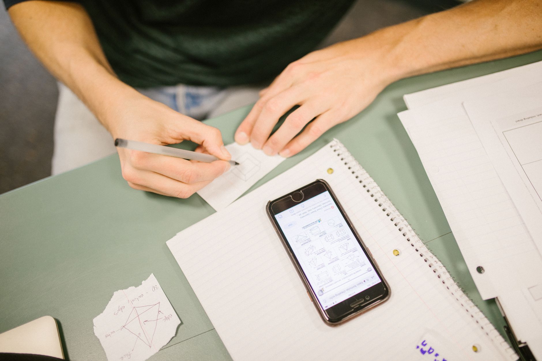 a smartphone screen displaying a vertical video feed of animated science diagrams and quiz prompts, resting on a wooden student desk beside a closed traditional textbook