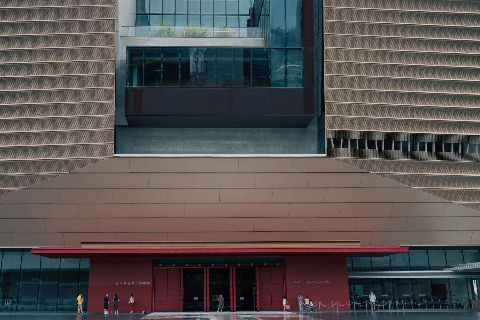 exterior of the Hong Kong Stock Exchange building on a clear morning, with the exchange's electronic ticker board visible in the lobby through glass windows