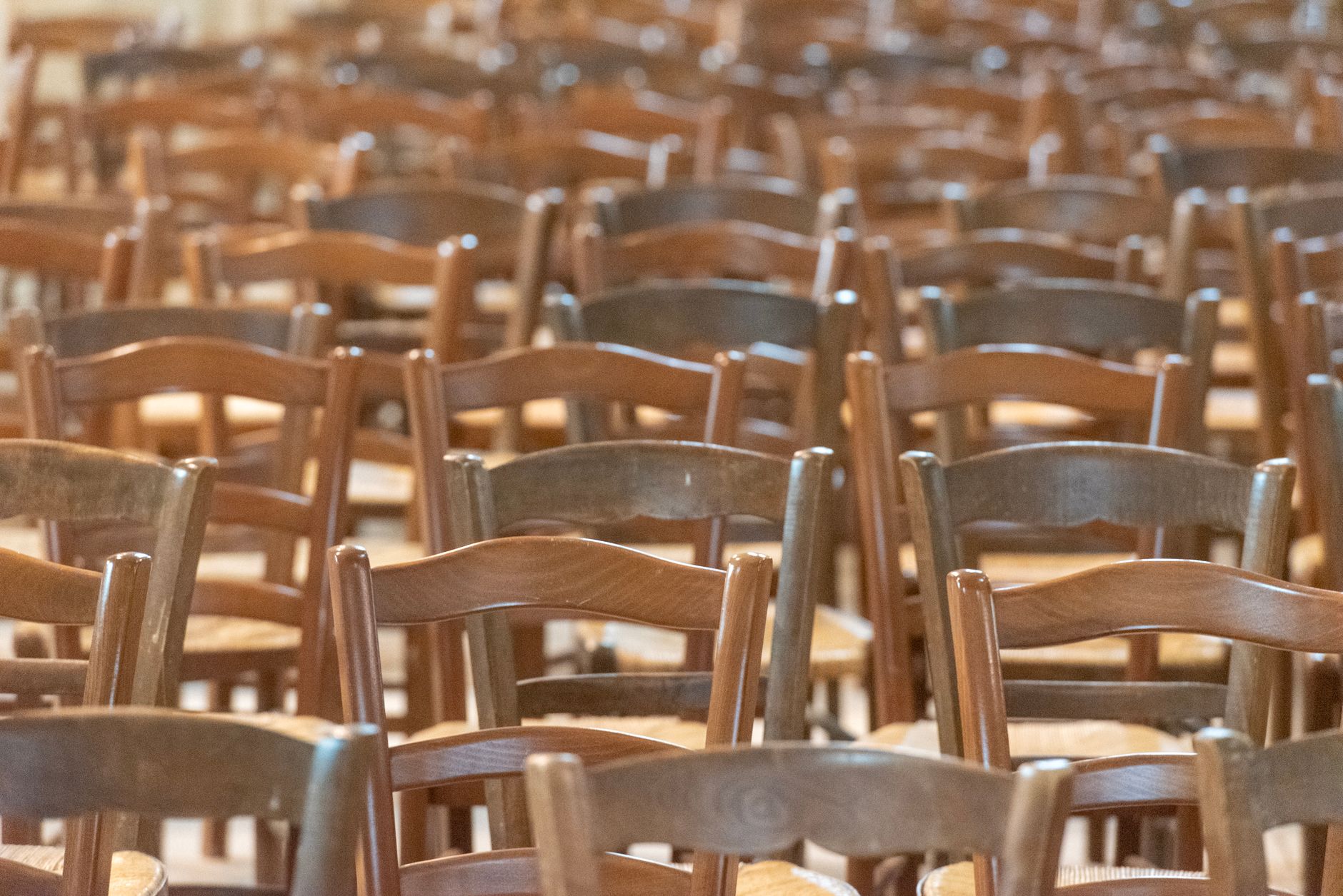 rows of worn wooden seats inside a grand but decaying civic auditorium, lit by harsh overhead lighting suggesting a government ceremony