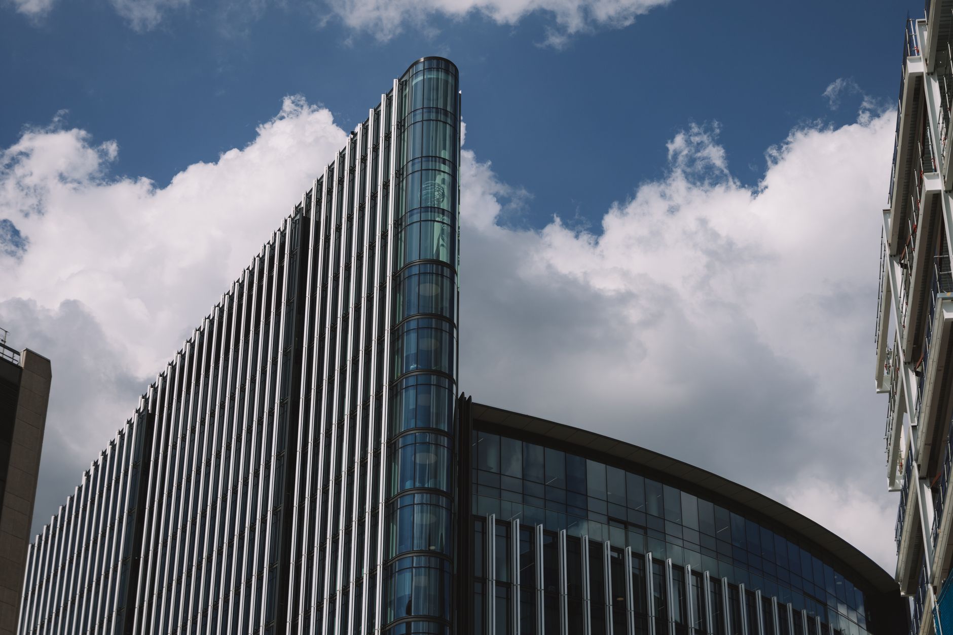 a wide-angle view of a London financial district office building exterior at midday, with digital advertising displays visible in the ground-floor windows