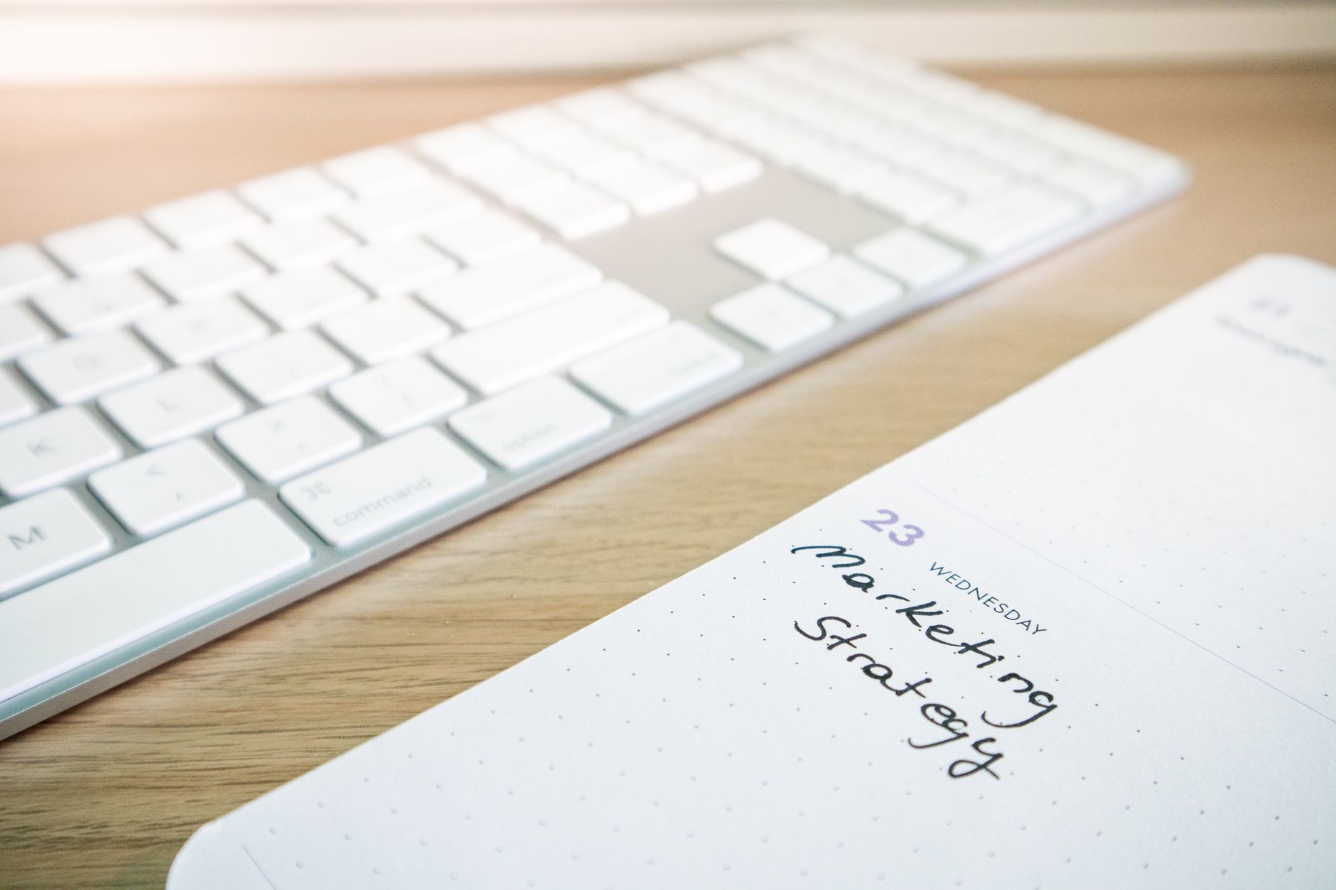 Close-up of a mechanical keyboard on a wooden desk beside a single open notebook with handwritten task items, soft studio lighting