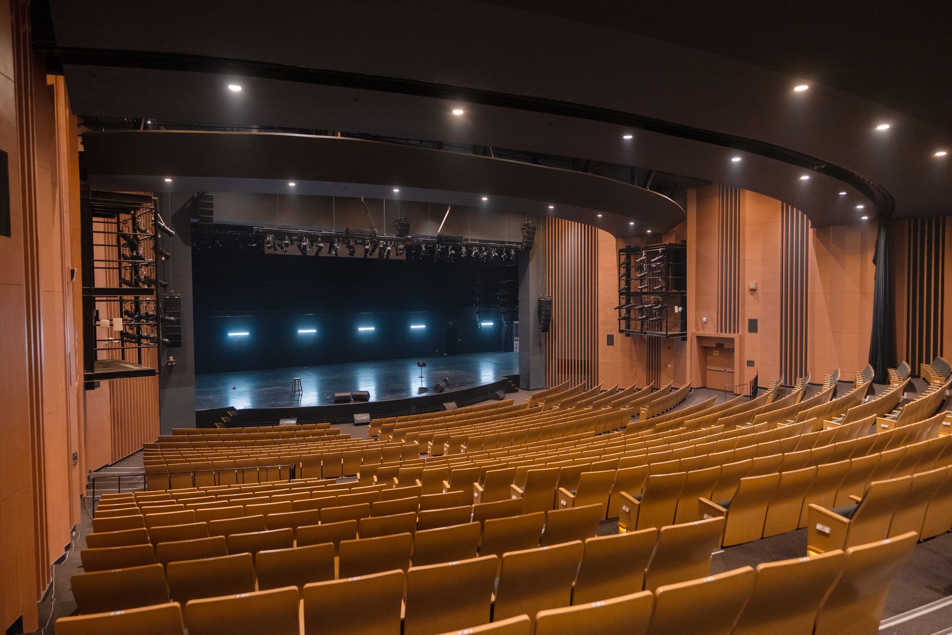 a large modern convention hall interior with rows of empty conference chairs facing a wide stage and floor-to-ceiling glass walls overlooking a city skyline at dawn