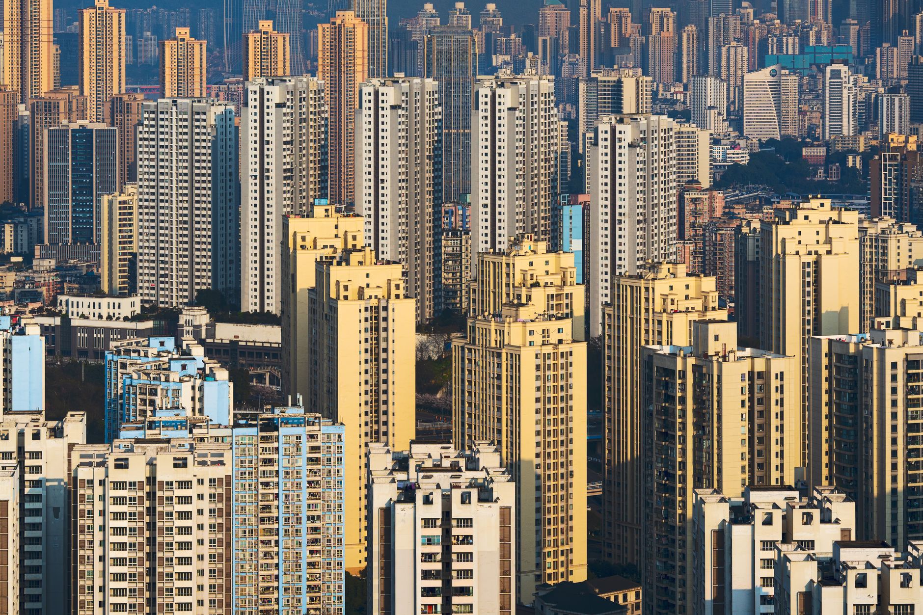 a wide aerial view of a dense urban skyline near a coastline at early morning, office towers lit from within against a pale sky