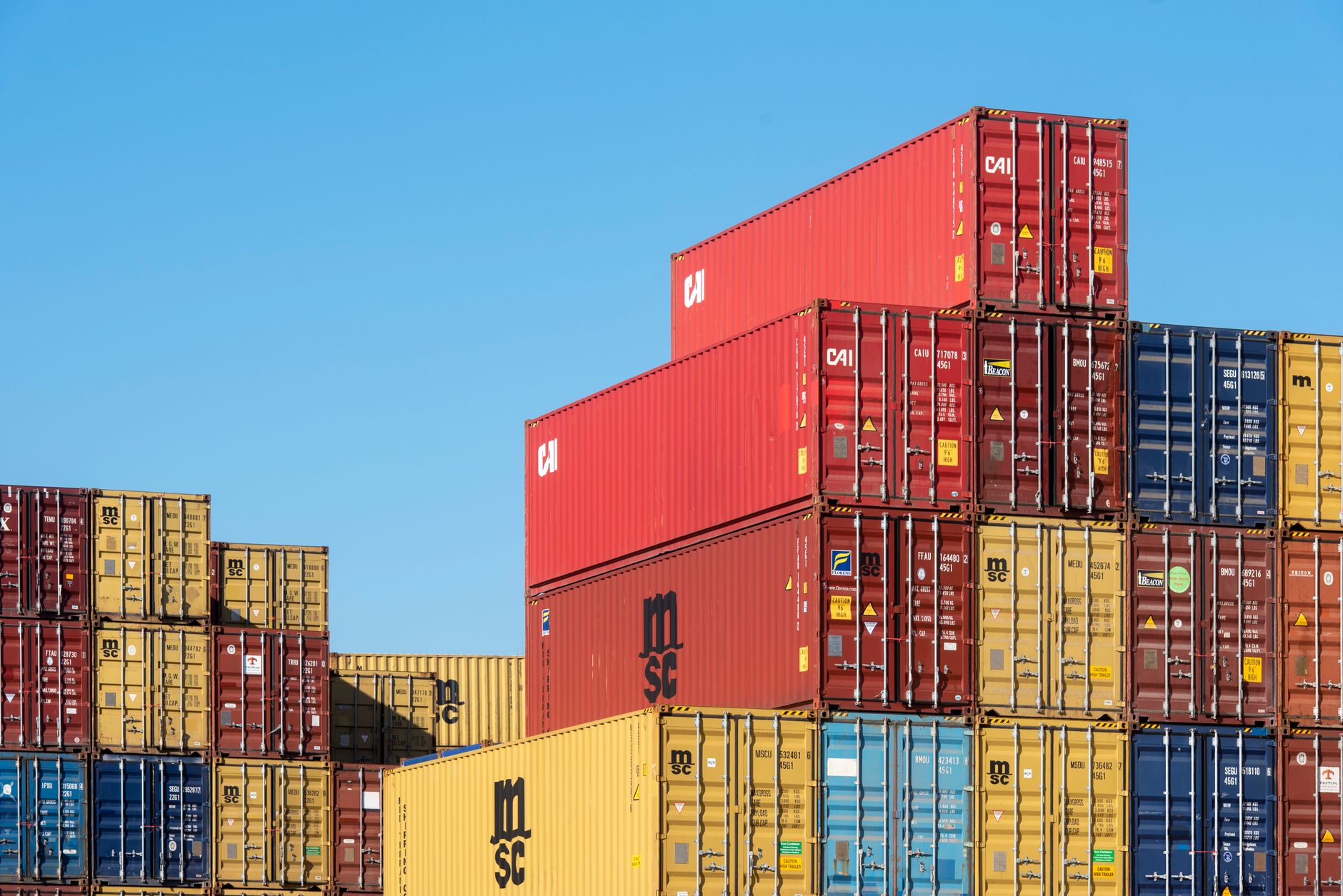 cargo shipping containers stacked at a busy international port terminal under overcast skies