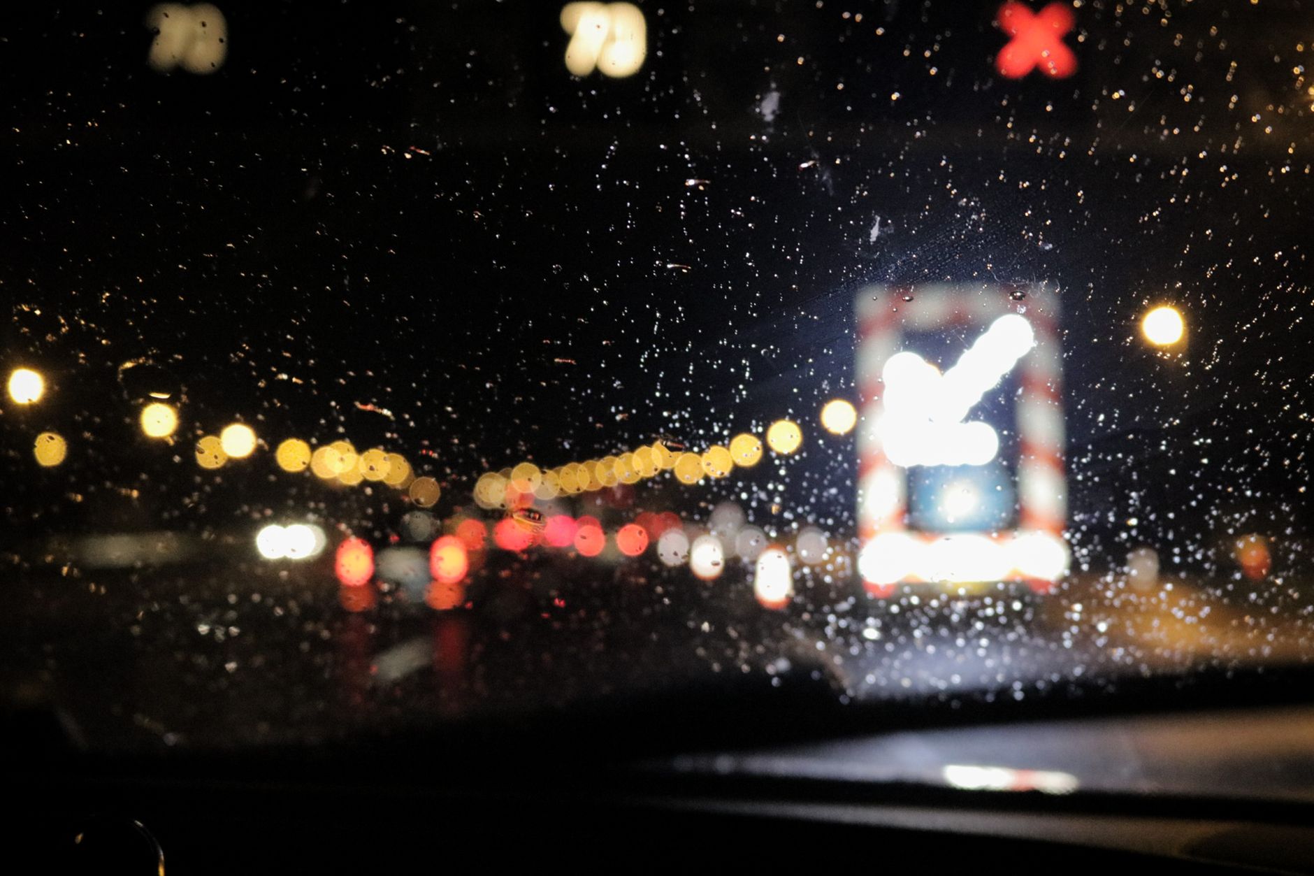 a self-driving vehicle moving through a rain-slicked city intersection at night, headlights illuminating wet pavement and traffic signals overhead