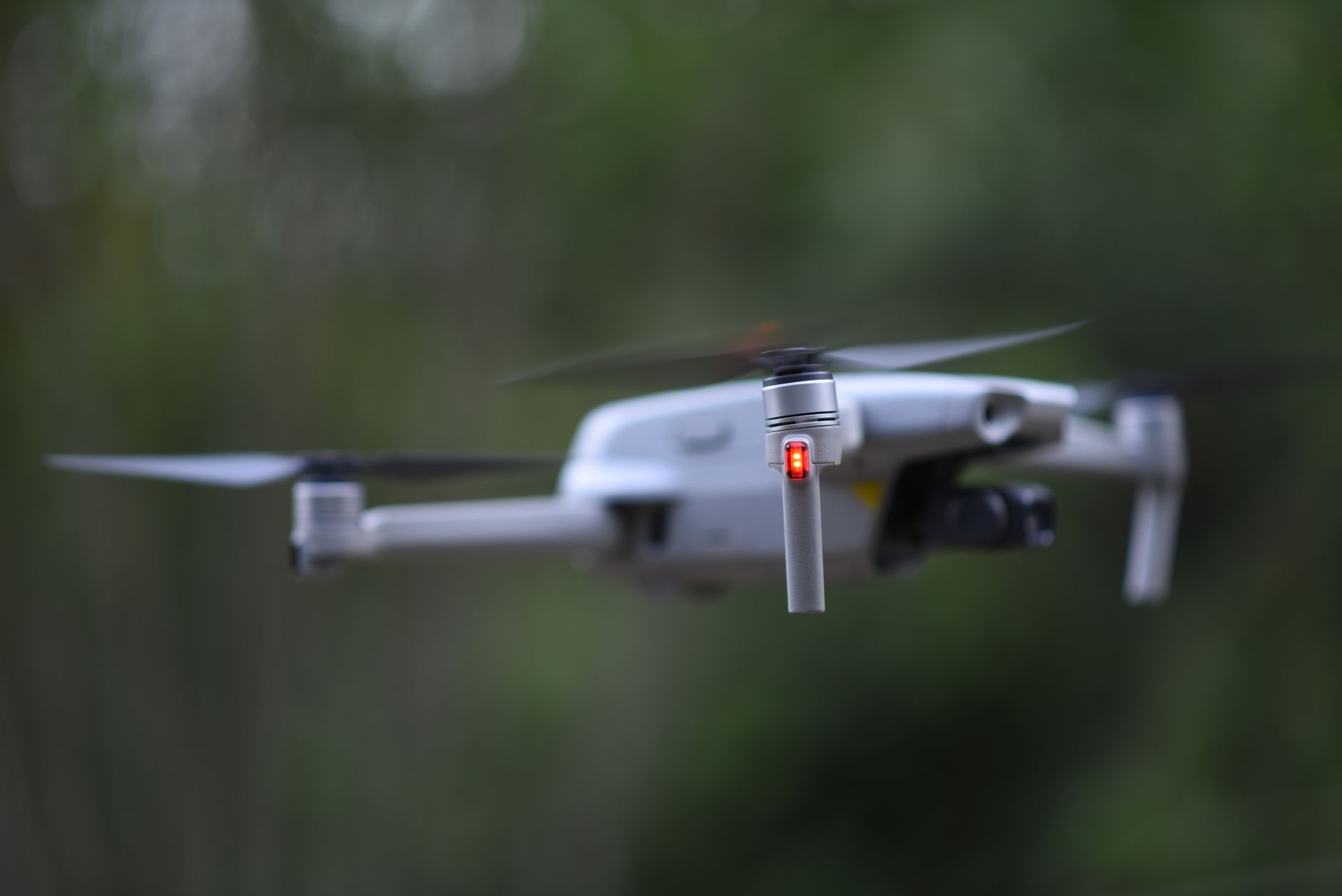 a compact autonomous drone hovering above an open industrial testing yard, rotors spinning, with sensor arrays visible beneath the frame