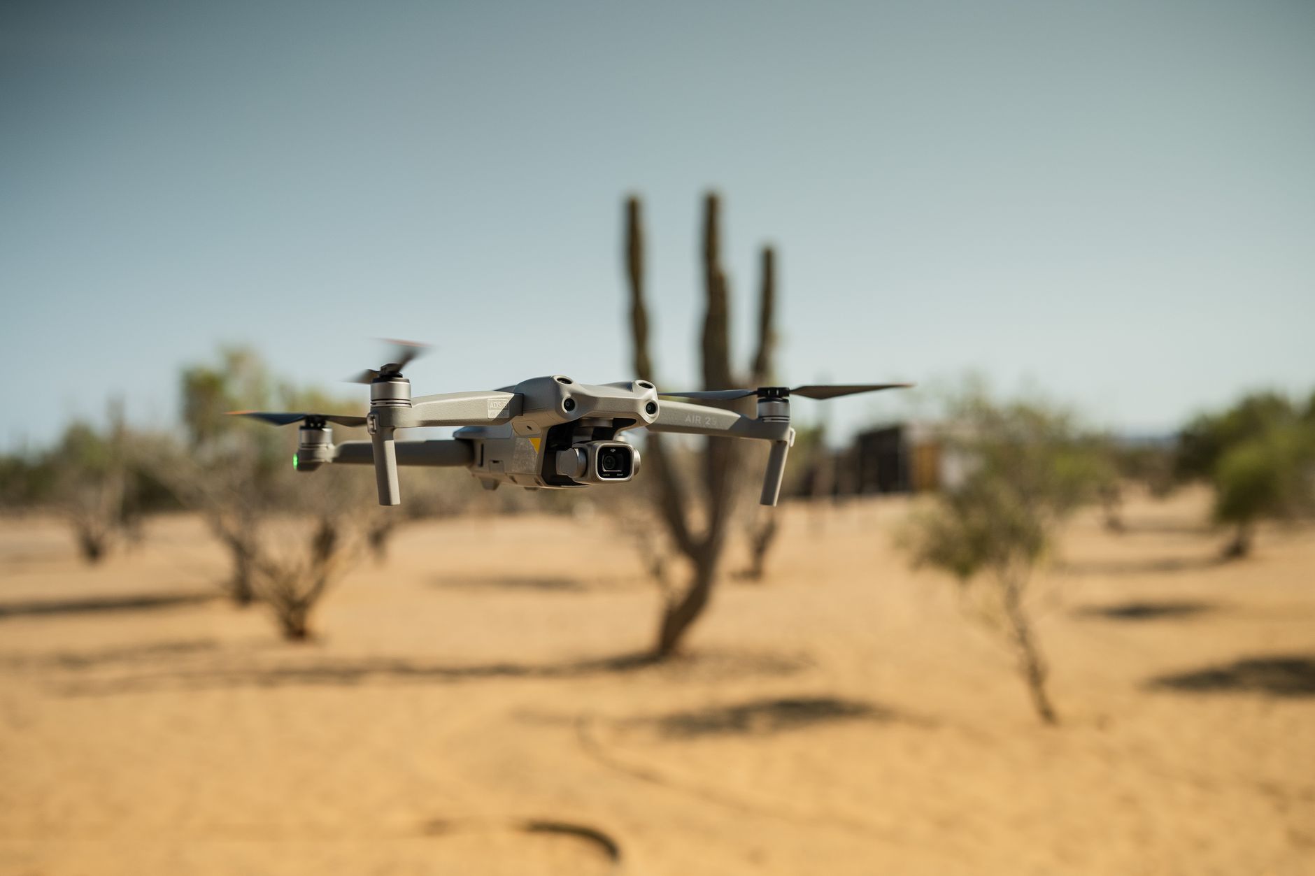 a compact military-grade autonomous drone hovering low over an open desert training ground at dusk, no crew visible