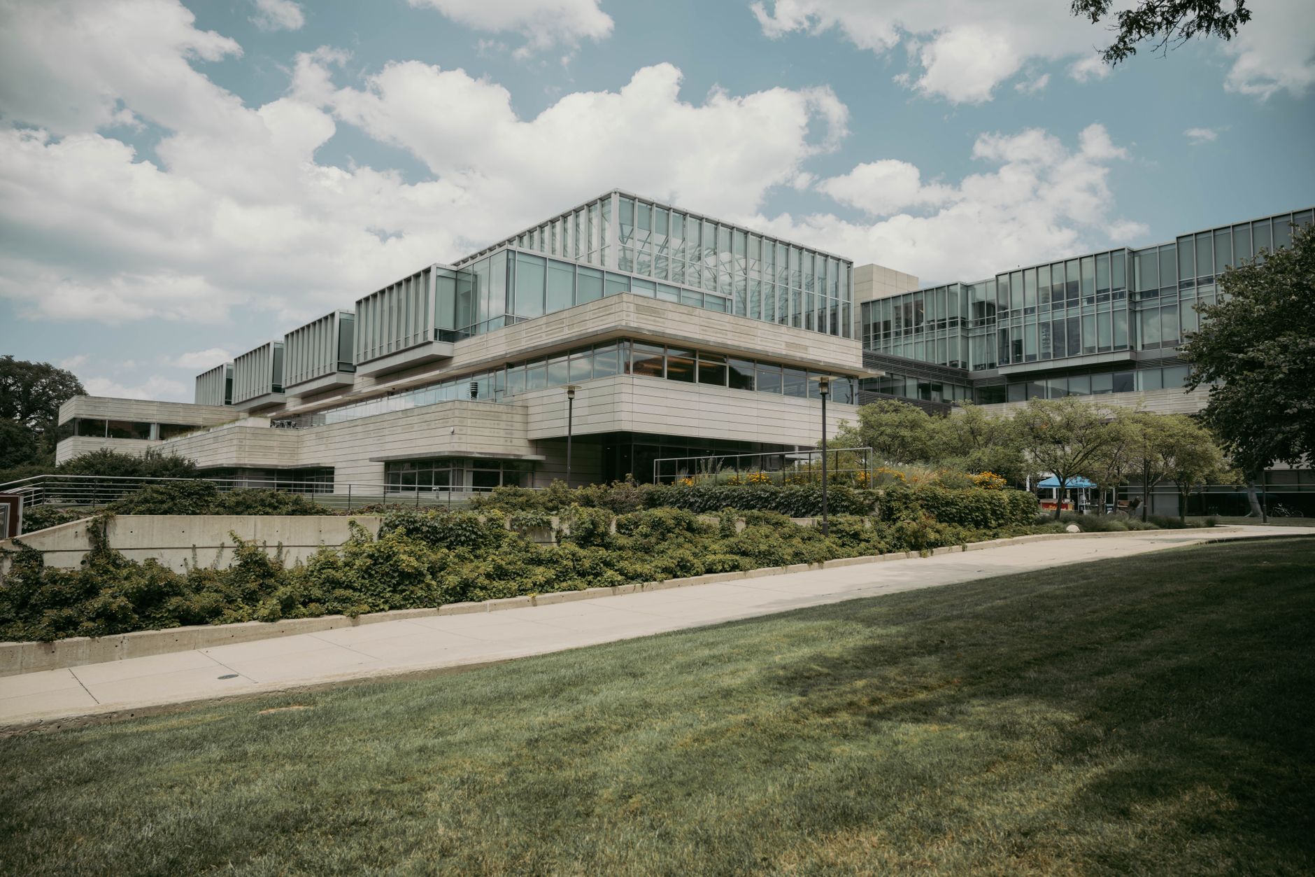 exterior of a low-rise modern office building with floor-to-ceiling glass facades reflecting afternoon sunlight, surrounded by neatly landscaped grounds in a technology campus setting