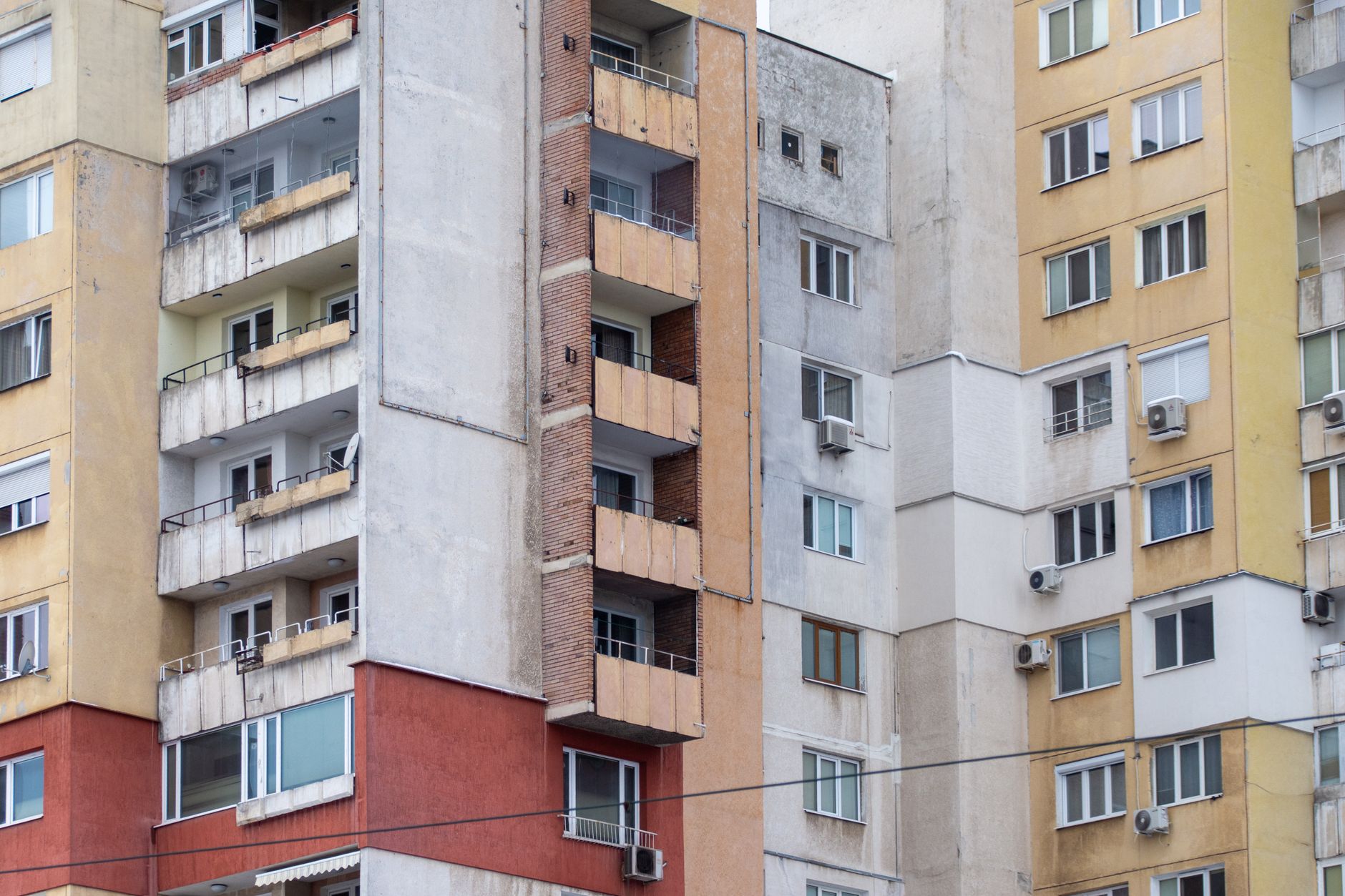 rows of smart electricity meters mounted on an exterior wall of a multi-story apartment building in a dense urban neighborhood, wires running along concrete