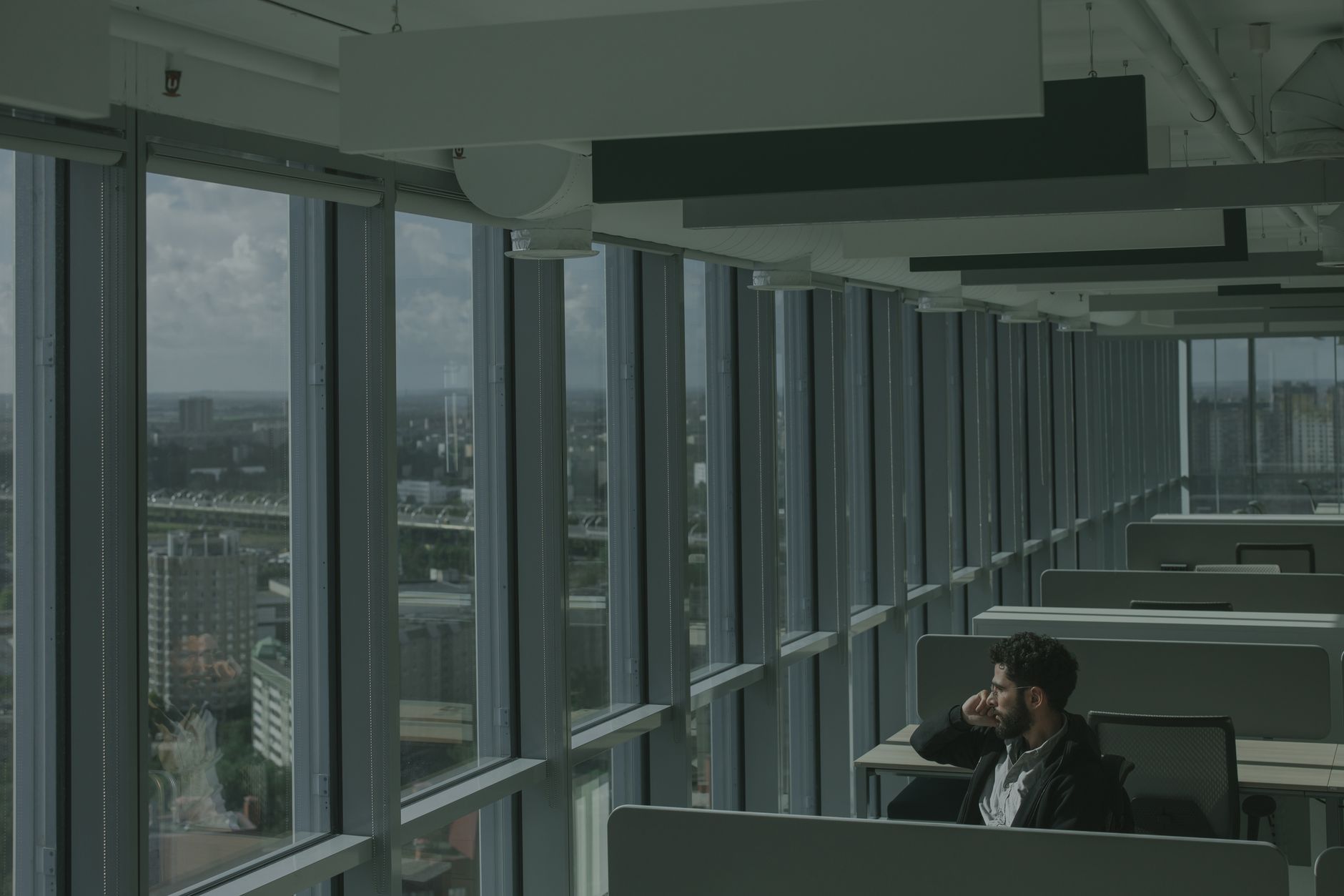 a wide-angle shot of a modern co-working space in a dense urban environment outside the United States, with floor-to-ceiling windows overlooking a city skyline, empty desks and whiteboards with diagrams visible