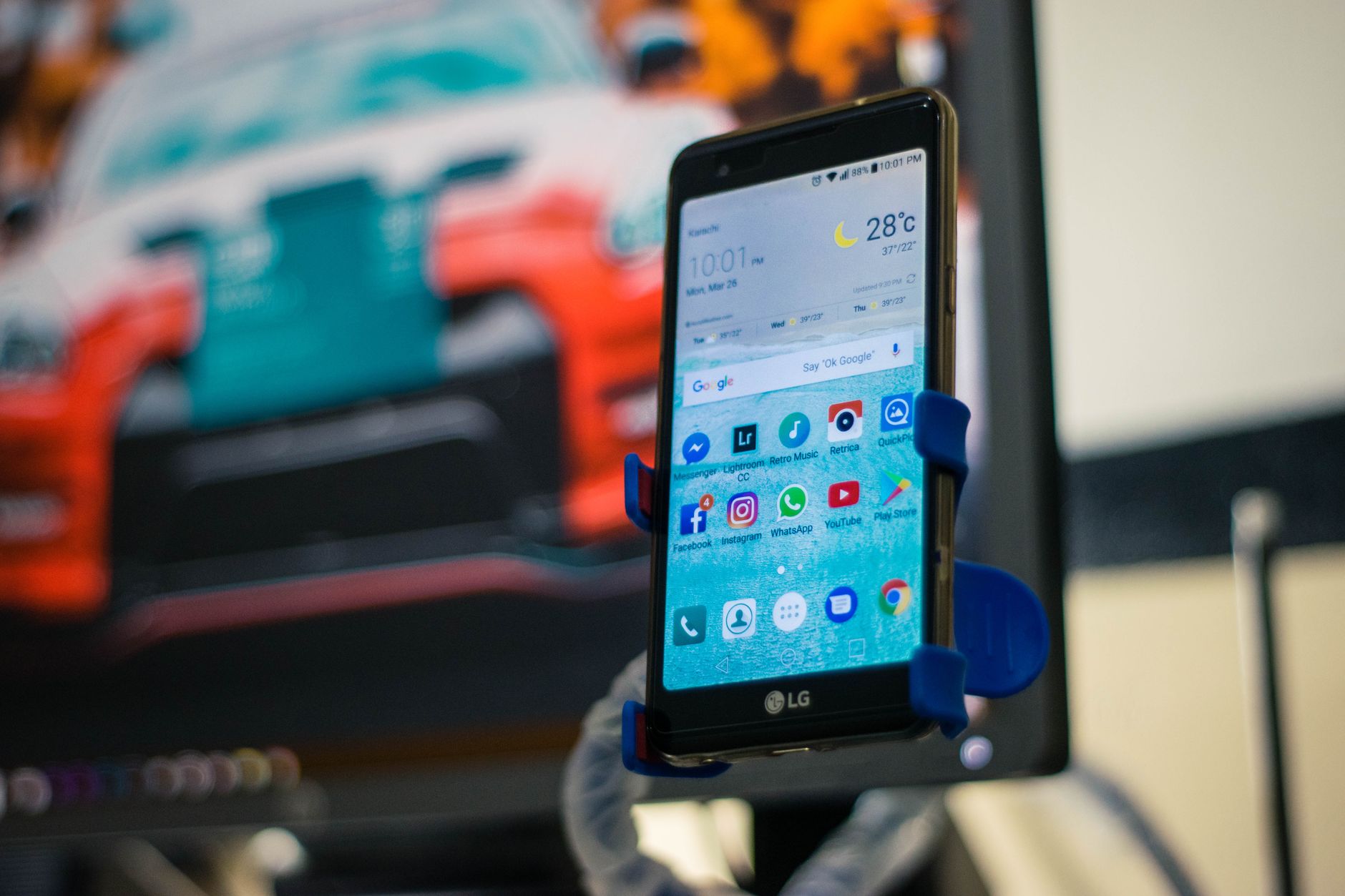 a slim Android smartphone propped upright against a stack of notebooks on a clean office surface, its display showing a mapping interface with satellite imagery