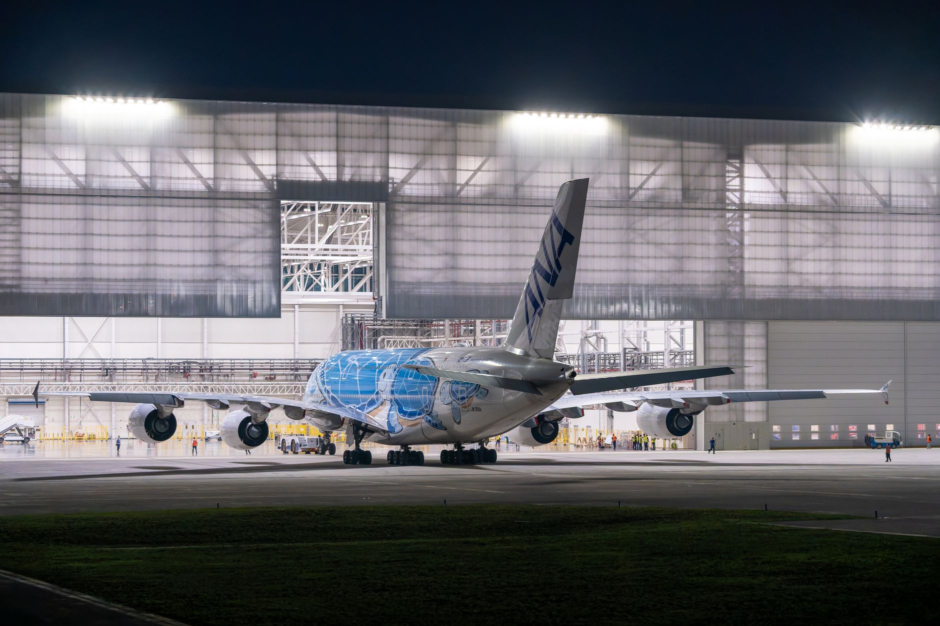exterior of a large aerospace manufacturing facility at dusk, with aircraft hangars and runway lights visible in the background