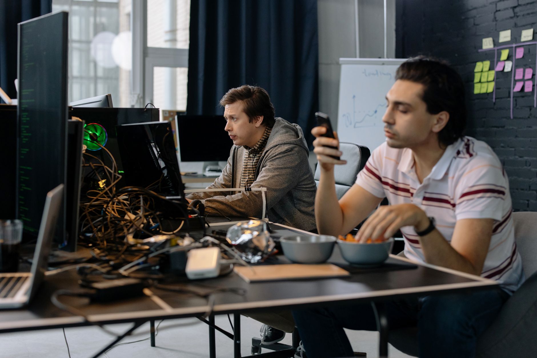 rows of workstations inside a modern startup office in a converted industrial building, monitors displaying code and data dashboards, exposed concrete ceilings and ambient lighting