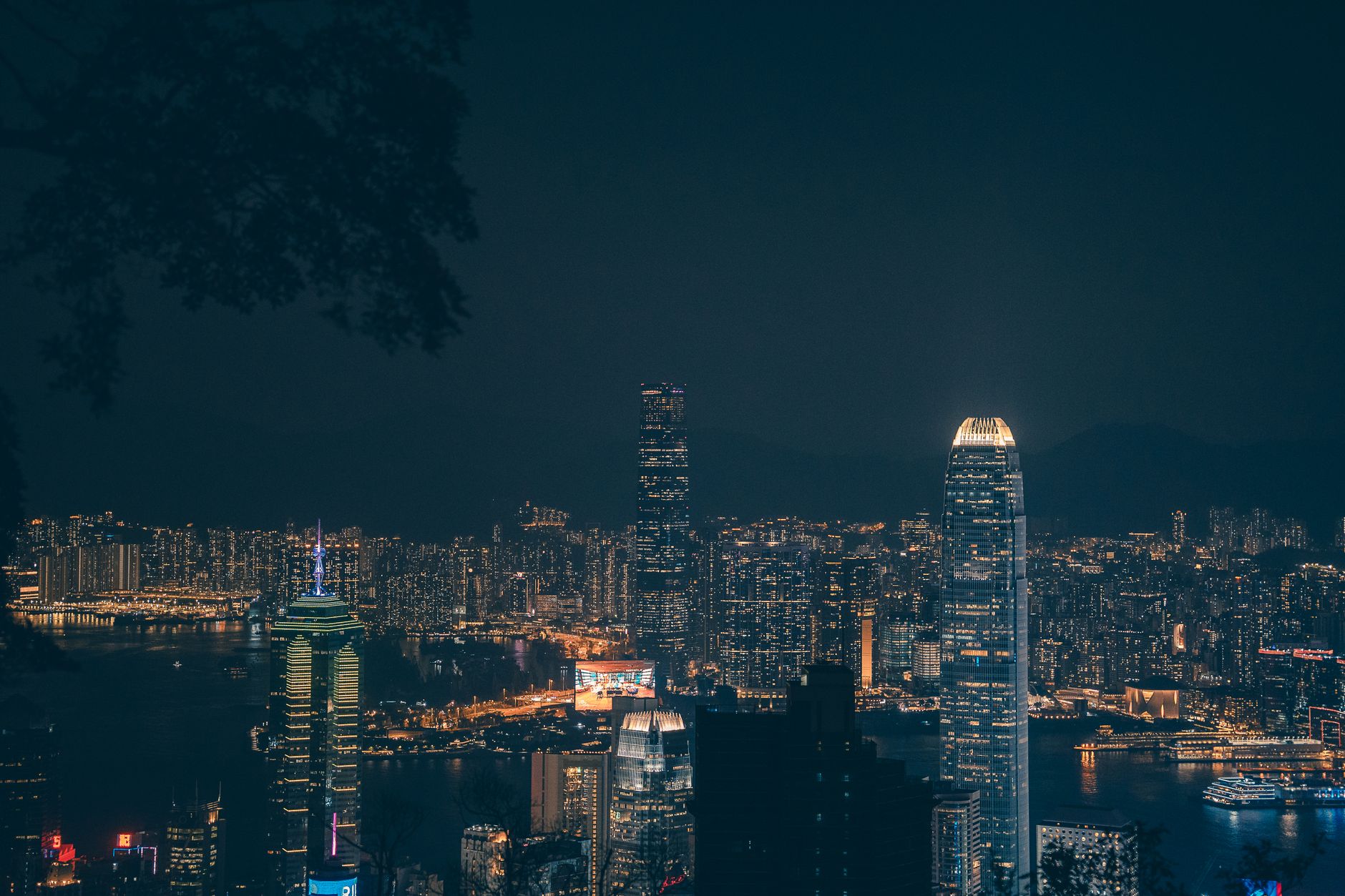 aerial view of the Hong Kong financial district skyline at dusk, glass towers reflecting golden light over Victoria Harbour, cargo vessels visible in the water below