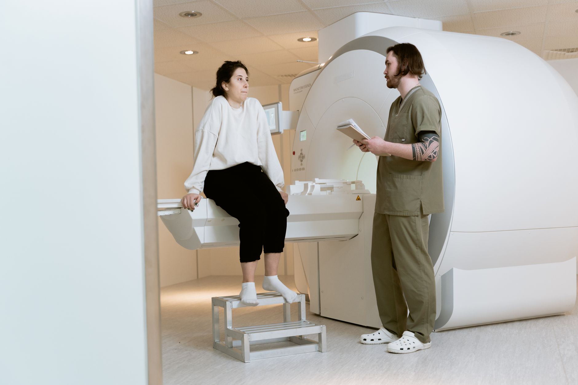 a sleek white cylindrical full-body scanning pod inside a minimalist clinical space with soft overhead lighting and bare white walls