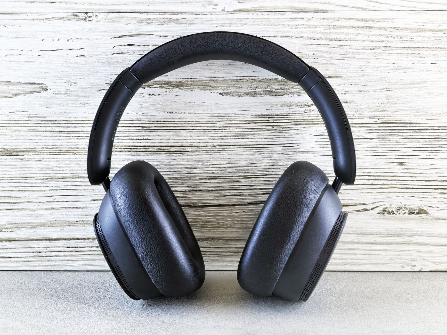 a close-up of a laptop open on a wooden desk next to a pair of over-ear wireless headphones, with soft window light in the background