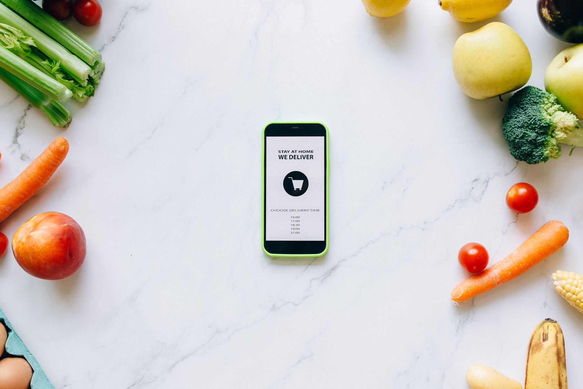 a smartphone resting on a kitchen counter with a food delivery app confirmation screen visible, beside a set of keys and a laptop partially open in the background