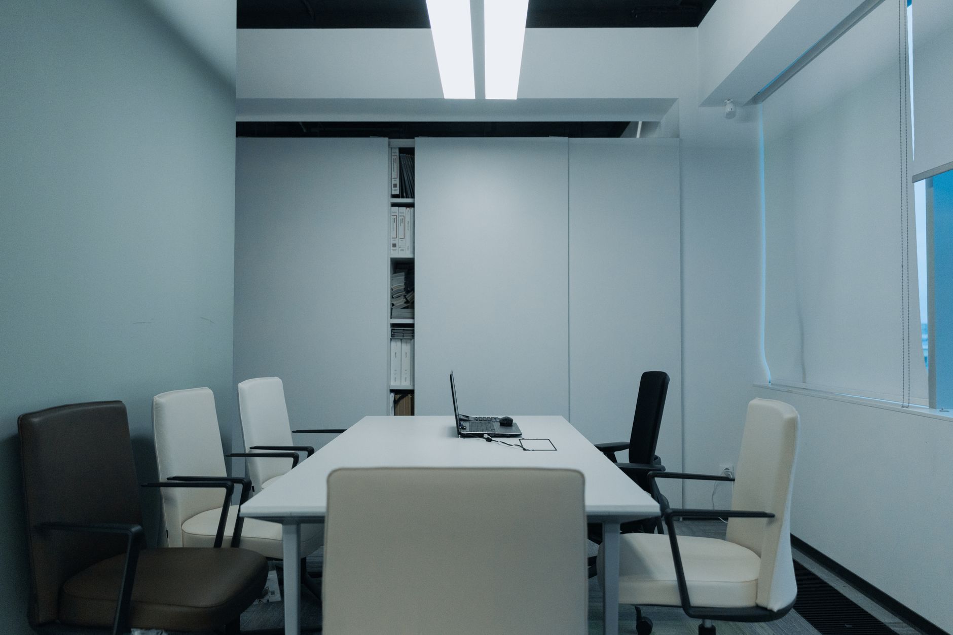 An empty executive boardroom with floor-to-ceiling windows overlooking a city skyline, leather chairs arranged around a long conference table, afternoon light casting long shadows across the surface