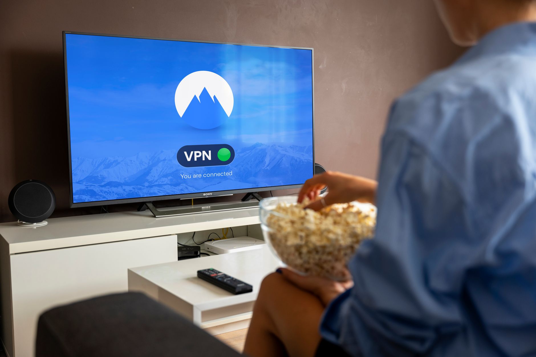 a large flat-screen television mounted on a living room wall displaying a streaming service selection menu, with a remote control resting on a wooden coffee table in the foreground