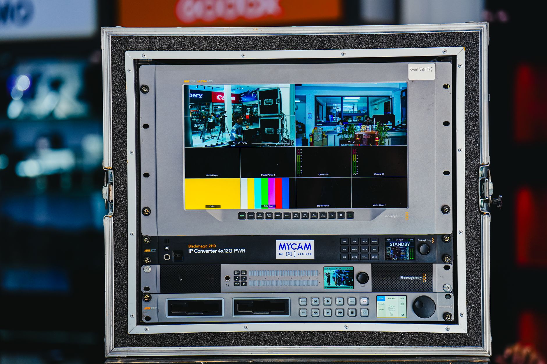 a tablet screen showing a streaming video interface with a sports broadcast paused mid-play, resting on a dark desk next to a pair of earbuds