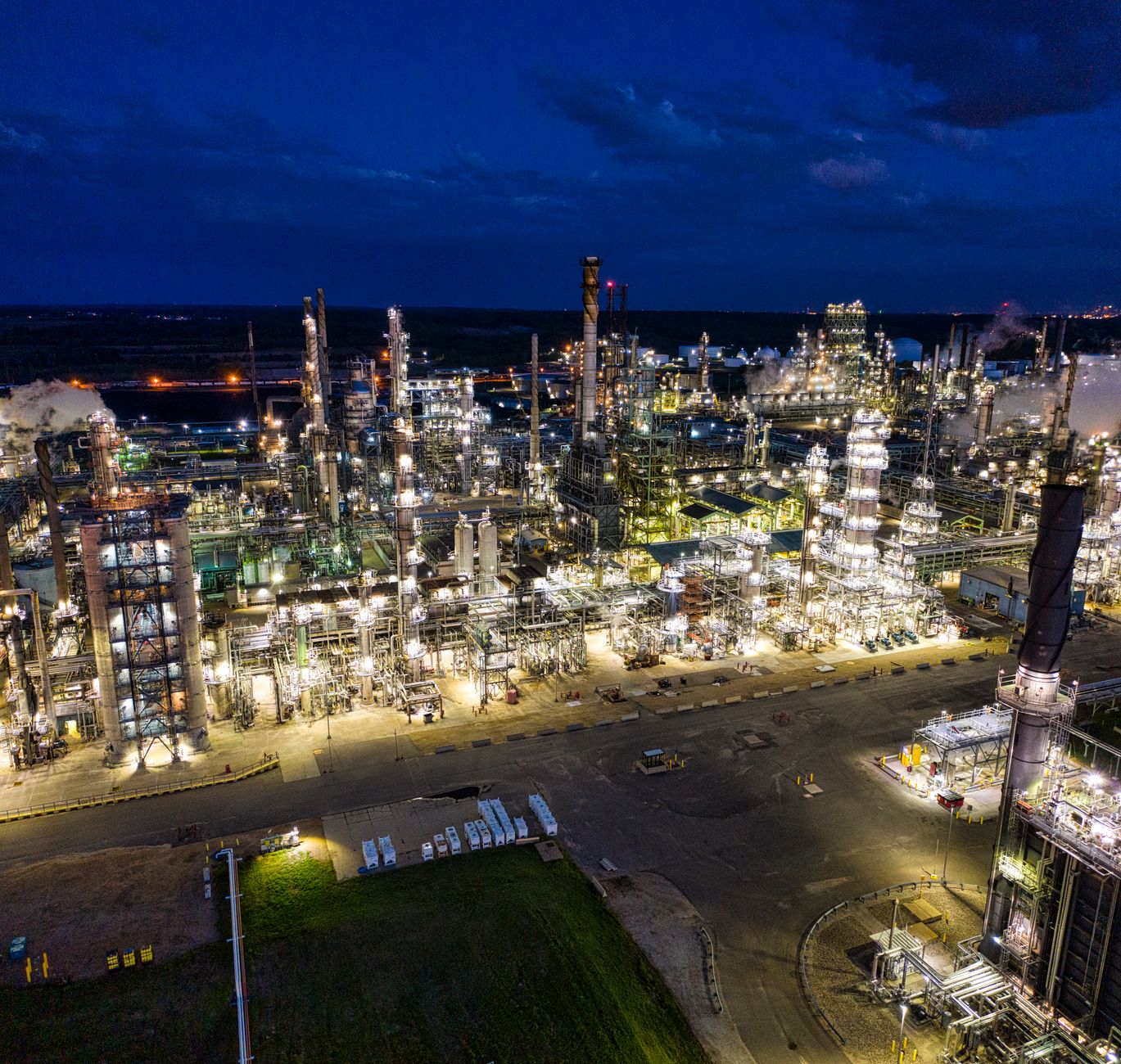 aerial view of a large natural gas pipeline corridor cutting through flat terrain at dusk, compressor stations visible at intervals