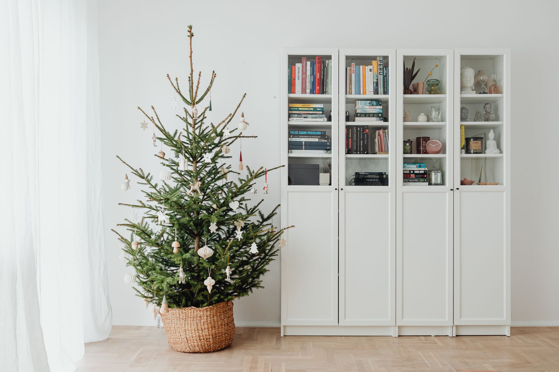a fully decorated artificial Christmas tree standing in a warmly lit living room corner, surrounded by wrapped gifts on a hardwood floor