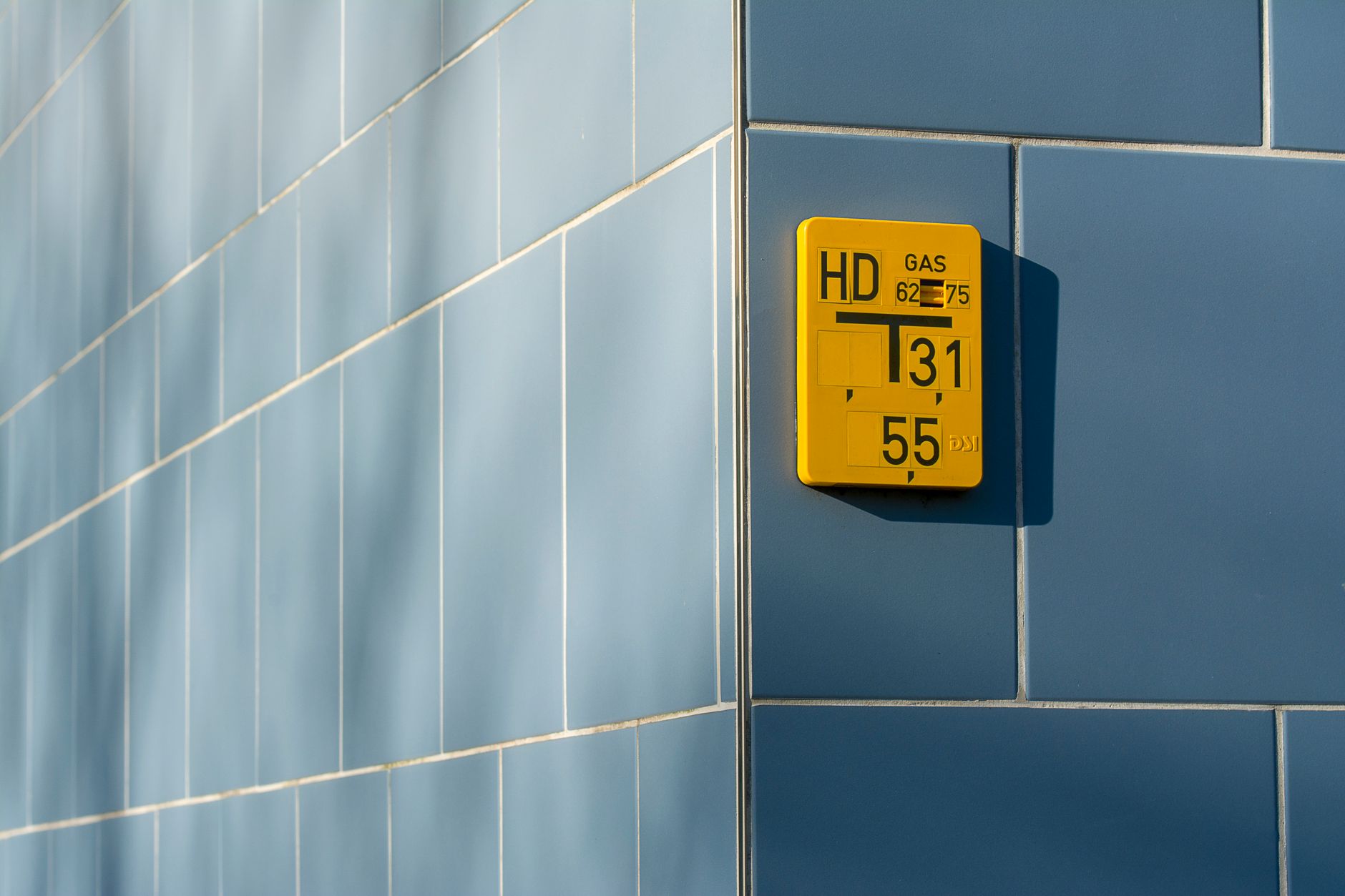 A close-up of a modern smart gas meter mounted on the exterior brick wall of a residential building, with a digital display and wireless antenna visible